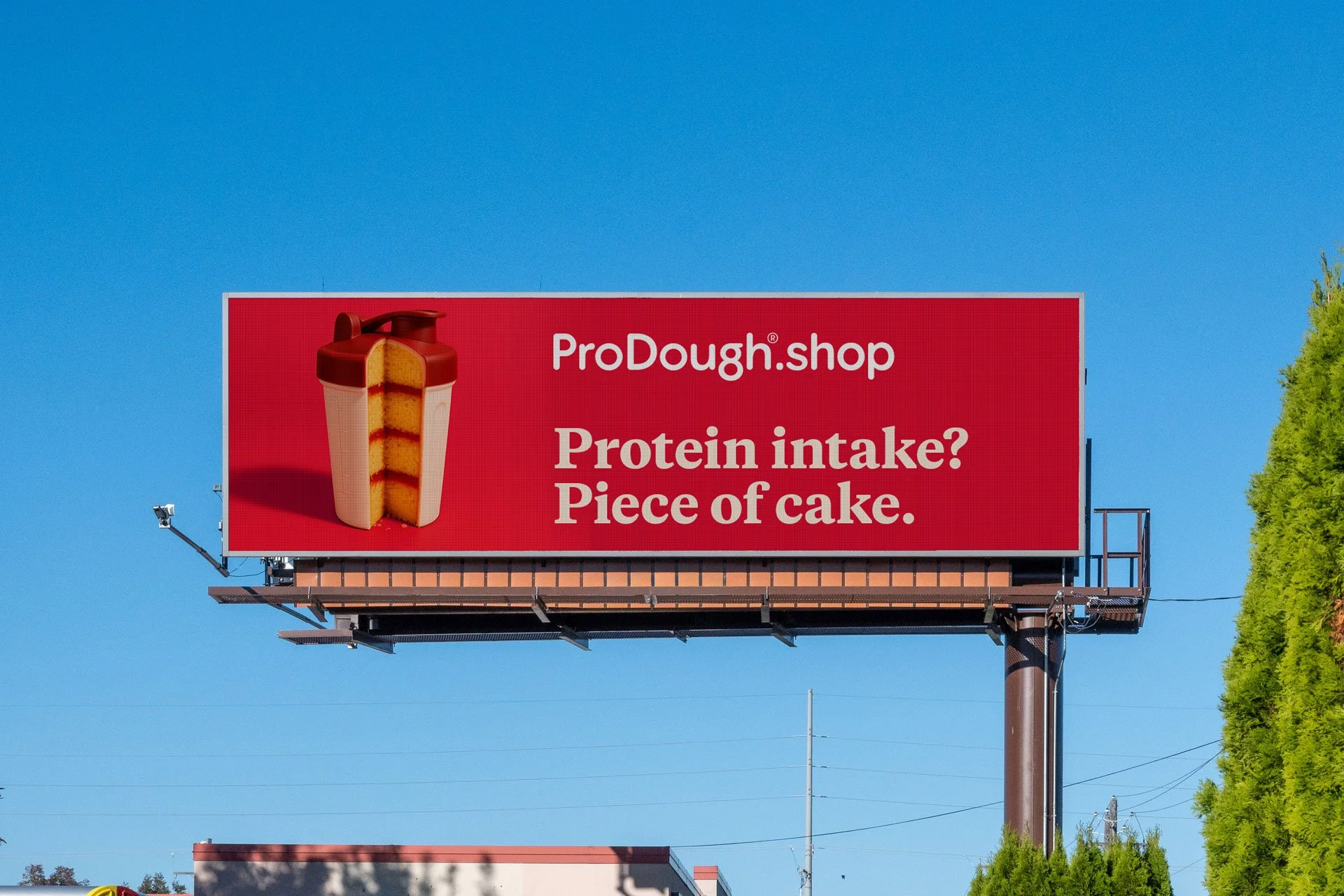 A billboard advertising ProDough.shop, showing a protein shake bottle with a cake inside, and the text 'Protein intake? Piece of cake.' against a clear blue sky.