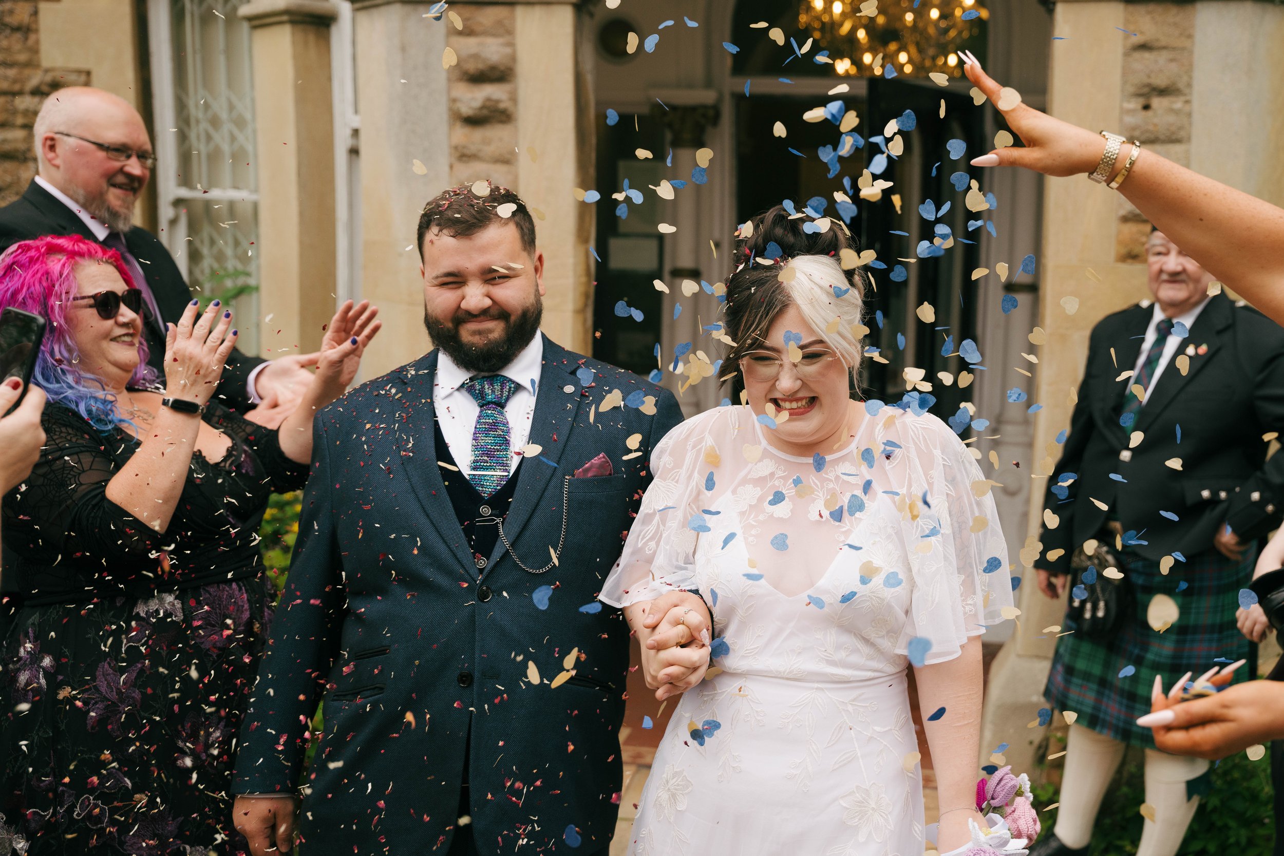 A Nottinghamshire wedding celebration with a bride and groom holding hands surrounded by guests, with confetti falling around them.