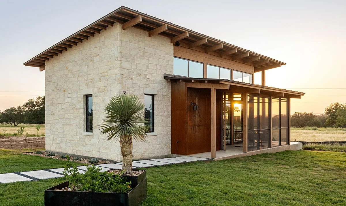 Modern Hill Country home with stone and wood exterior, large windows, and a screened porch at sunset in Hye Springs Ranch in Fredericksburg TX.