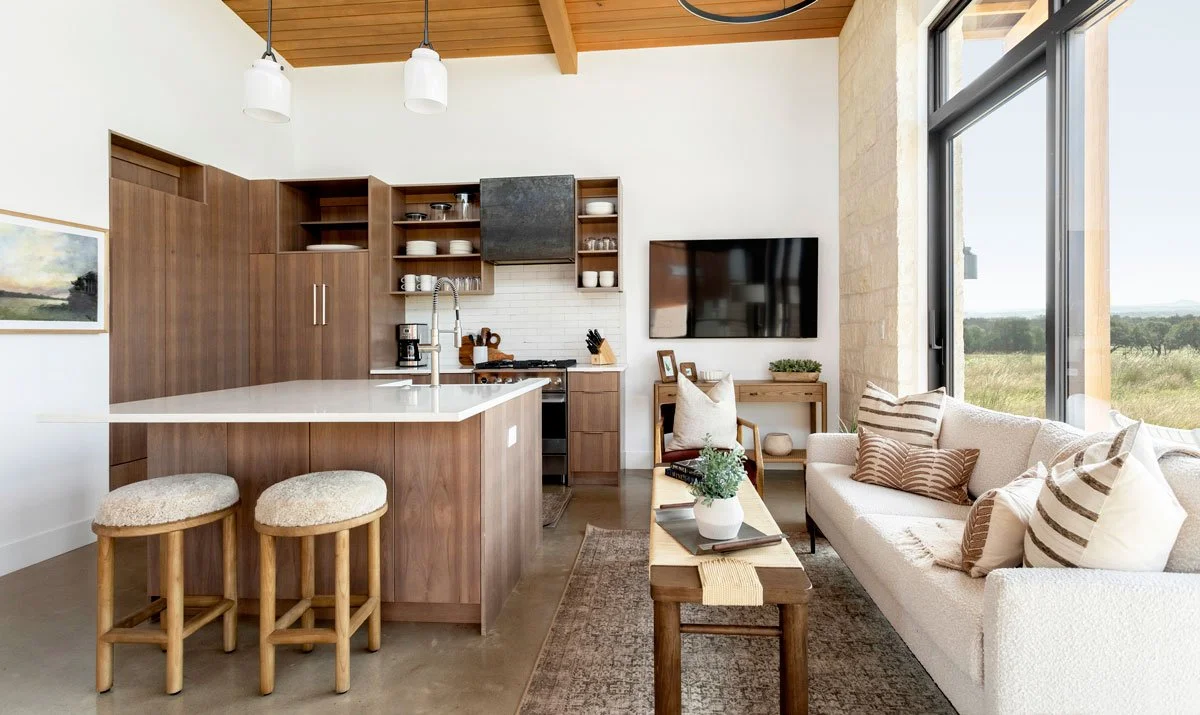 Open concept living room and kitchen with wood accents, large windows, and modern seating in Hye Springs Ranch in Fredericksburg TX.