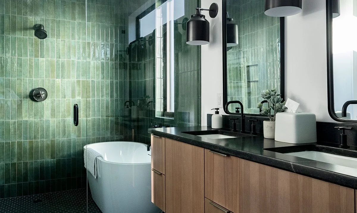Modern bathroom in Hye Springs Ranch homes with green tiled shower area, black fixtures, double sink vanity, and large mirror in Fredericksburg TX.