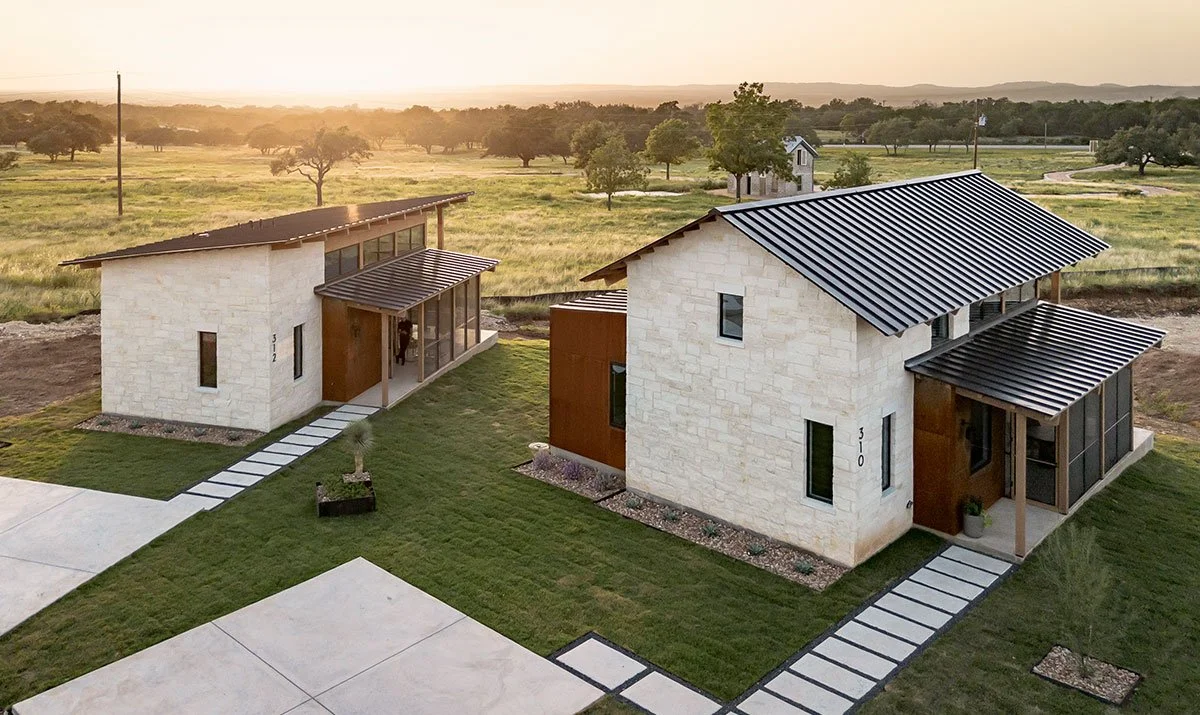 Two modern Hill Country style homes with white stone exteriors and metal roofs at sunset in Hye Springs Ranch in Fredericksburg TX.