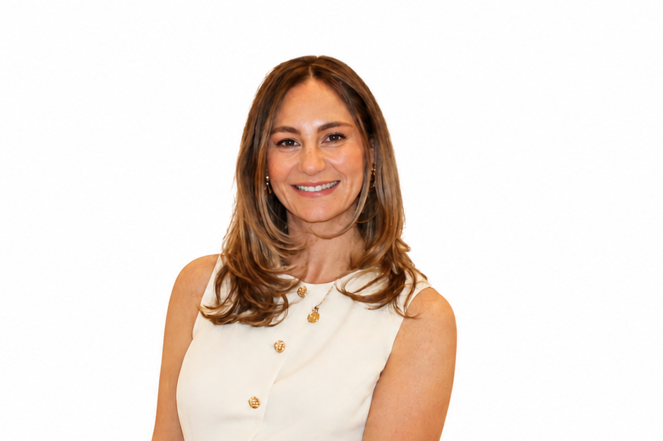 A woman with shoulder-length light brown hair smiling, wearing a sleeveless cream-colored top with gold buttons, gold jewelry, against a plain white background.
