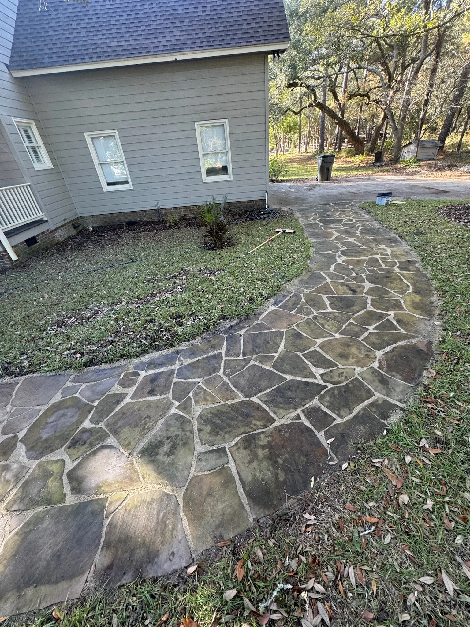 stone walkway leading to a house with siding, surrounded by grass and trees