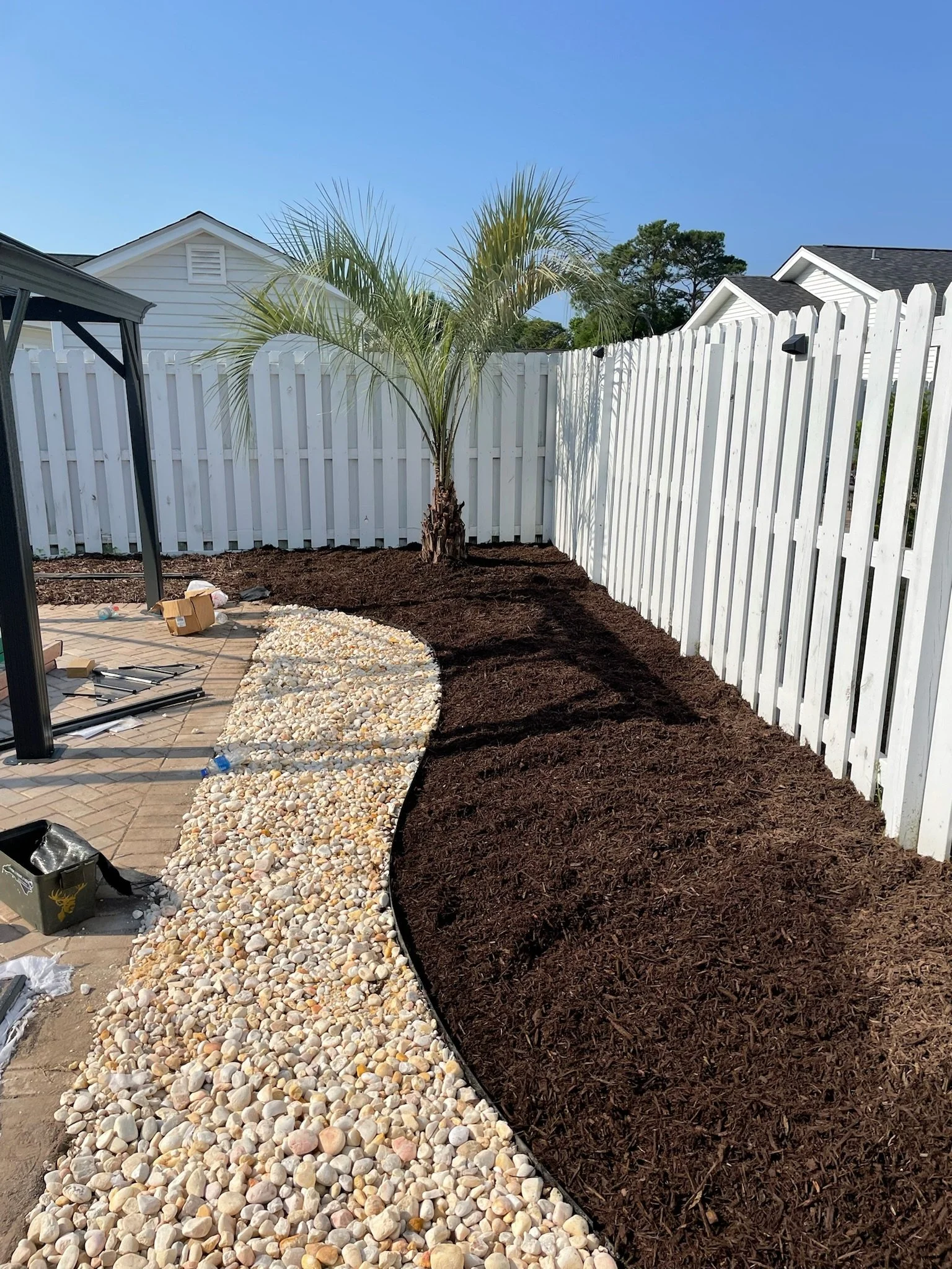 Garden path with white stones and palm tree near white picket fence