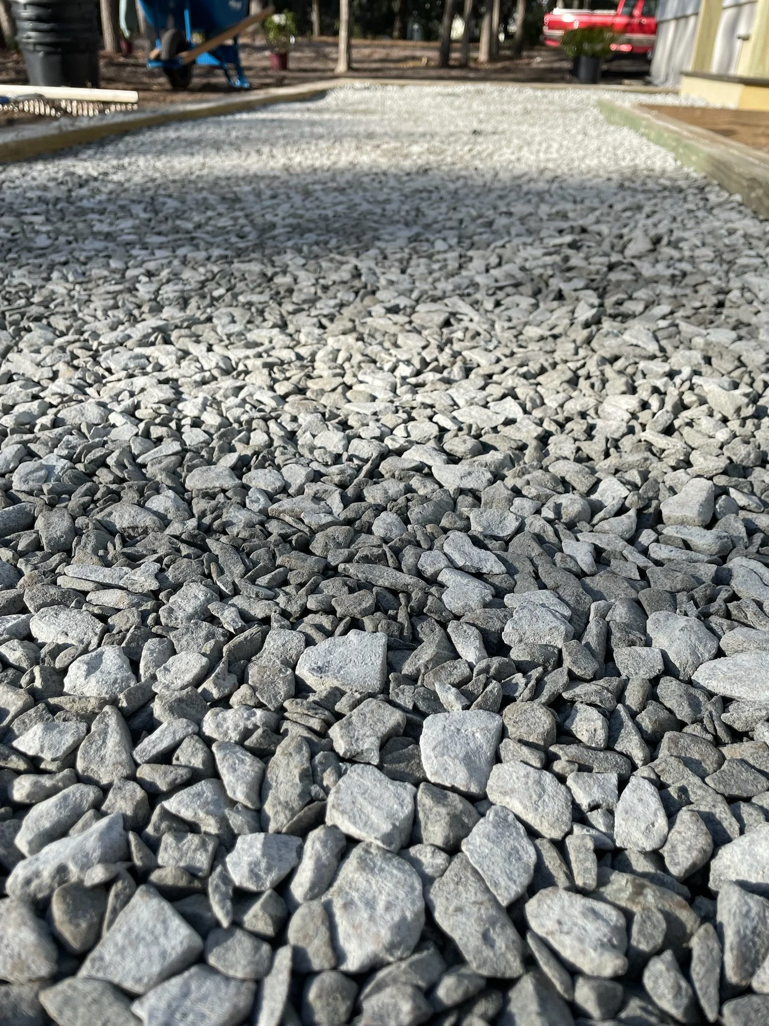 Close-up of gray gravel pathway with blurred background showing a garden setting.