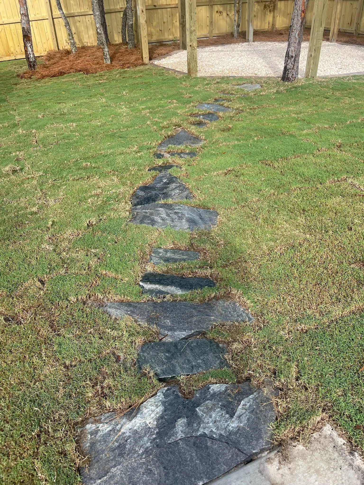 Stone pathway on grass lawn with wooden fence and trees