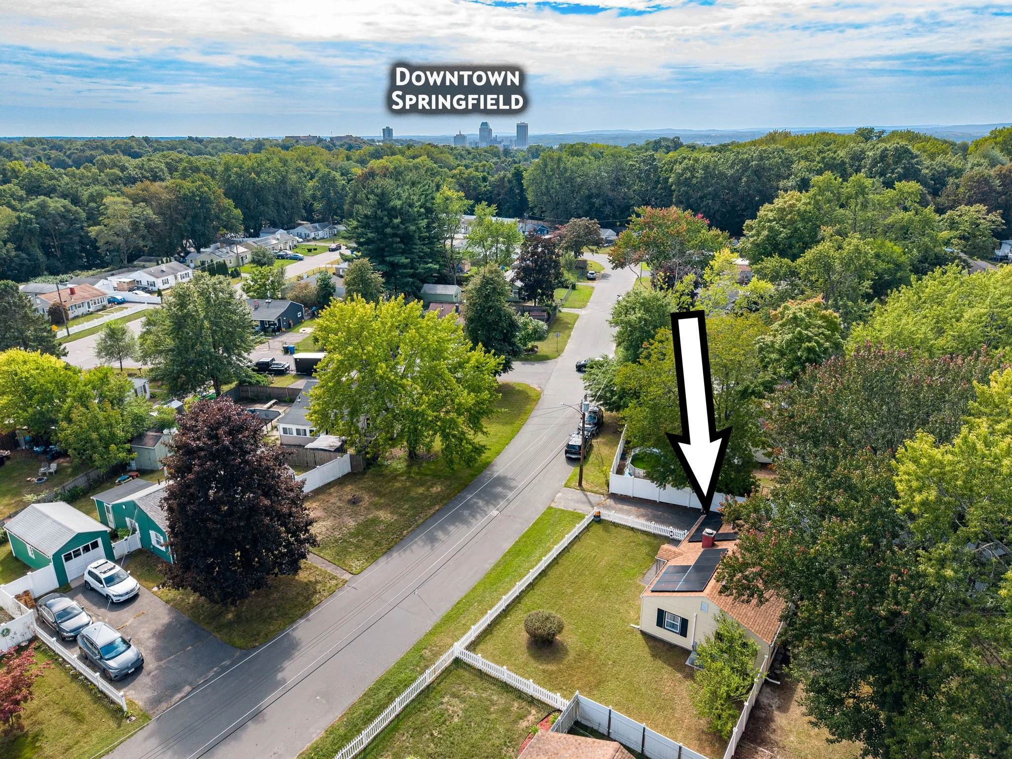 An aerial view of a suburban neighborhood with houses, trees, and a street. In the background are high-rise buildings in downtown Springfield.