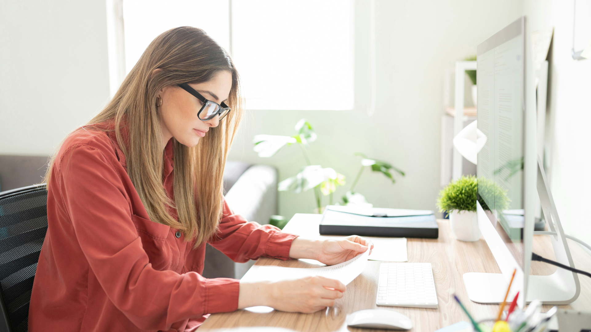 Woman reading a book at her desk in a bright office.