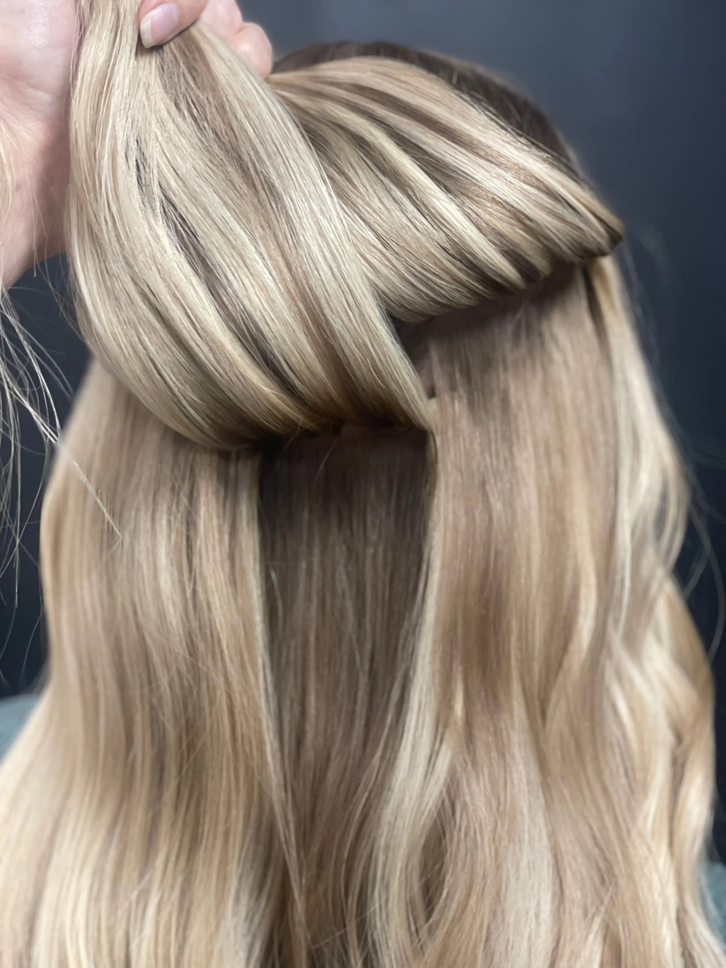 Close-up of a person's blonde, wavy hair with a small section being lifted by hand.
