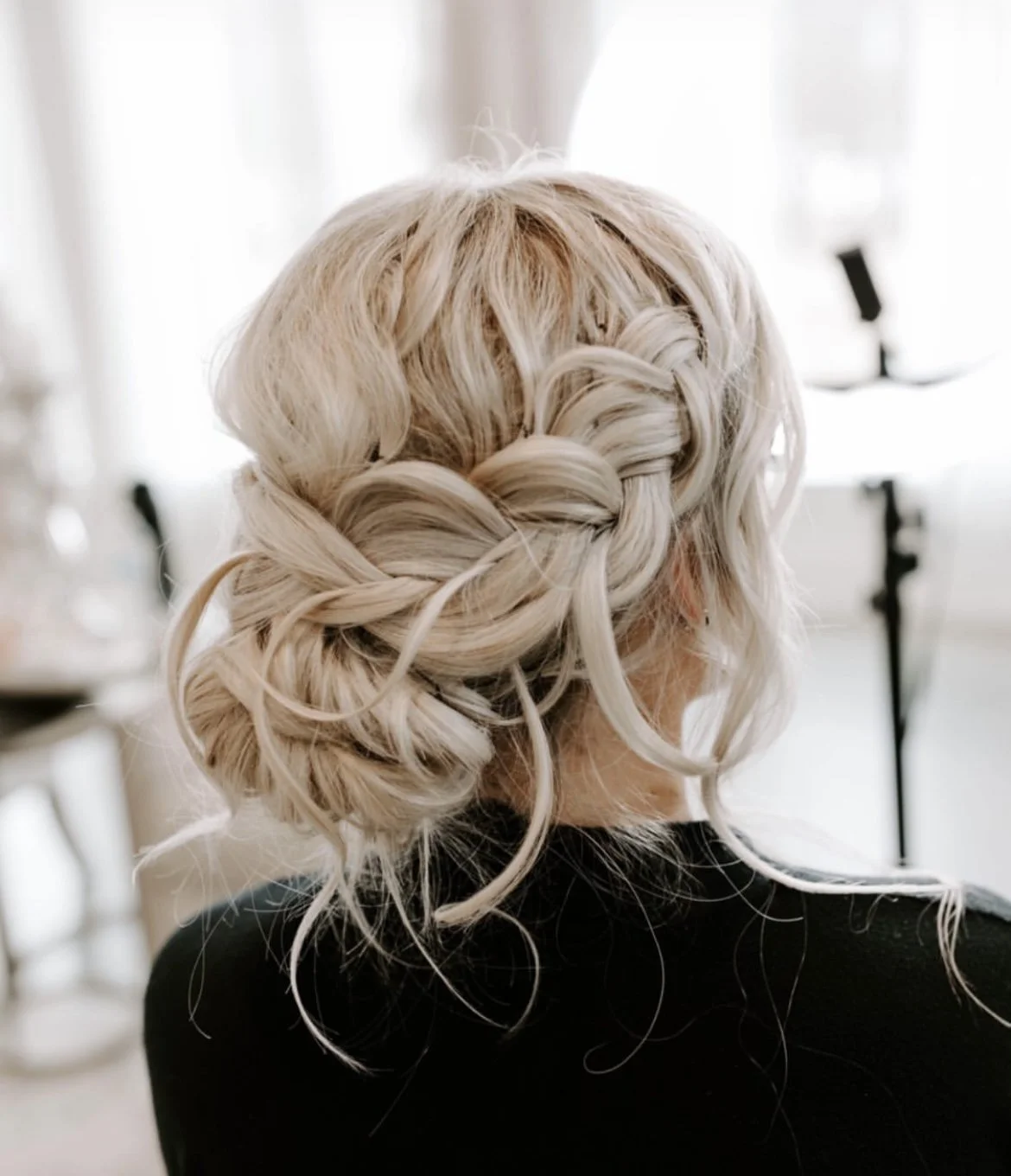 Back view of a woman with platinum blonde hair styled in an intricate braid updo with loose curls.