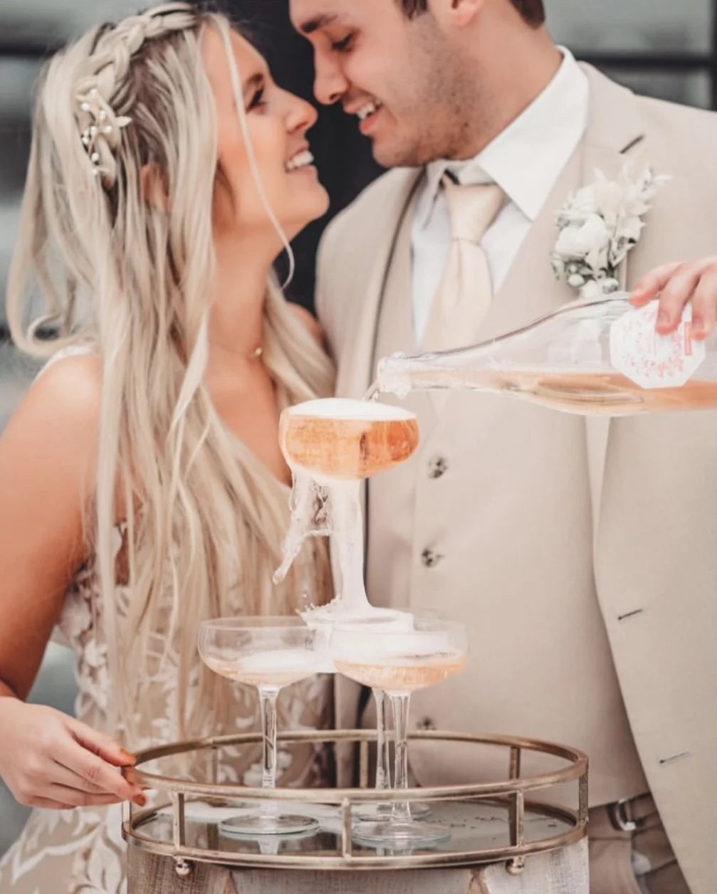 Bride and groom pour champagne into a tower of glasses at their wedding celebration, smiling and close to each other.