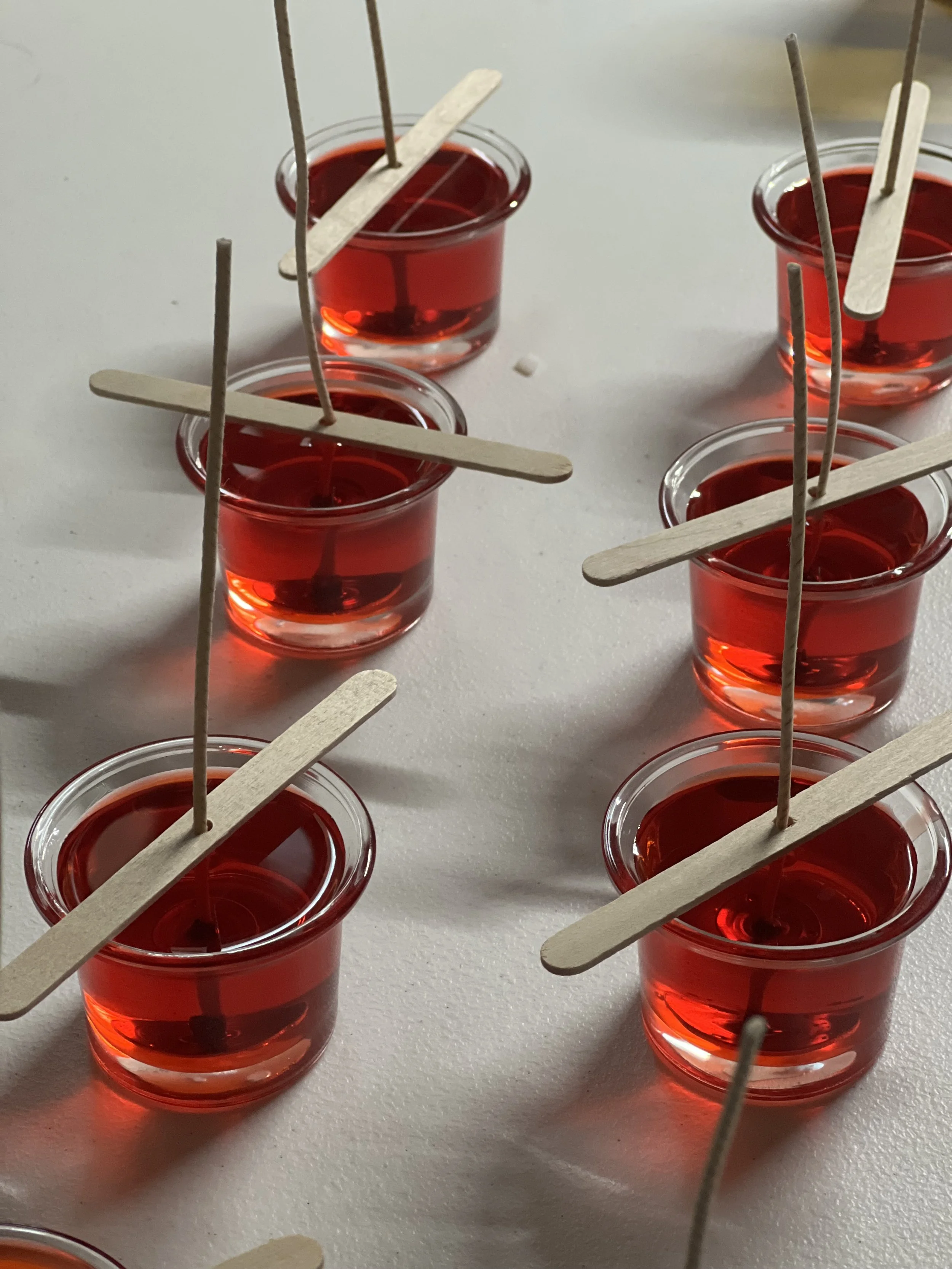 Small clear plastic cups filled with red liquid, each with a wooden stir stick and a toothpick inserted upright, arranged on a white surface.