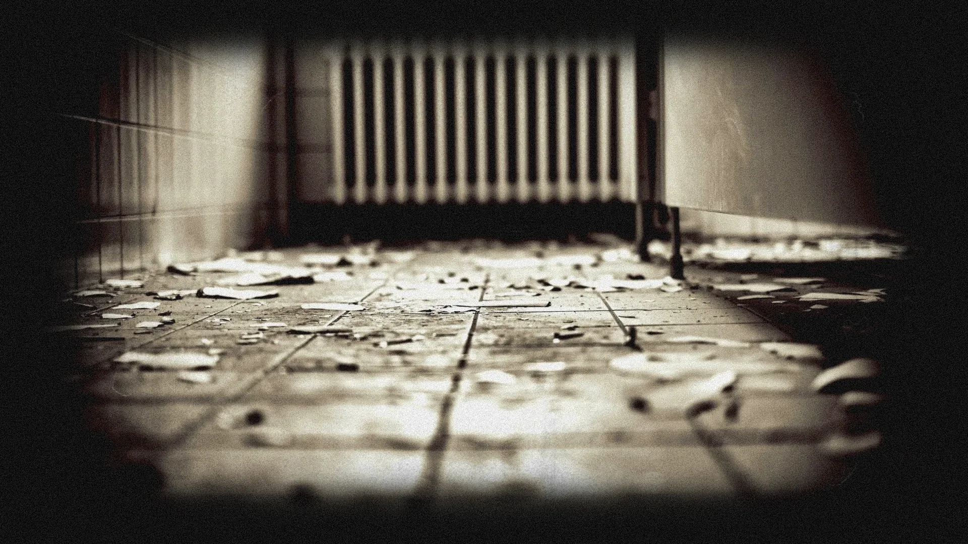Abandoned room with broken tiles on the floor and a radiator against a wall.