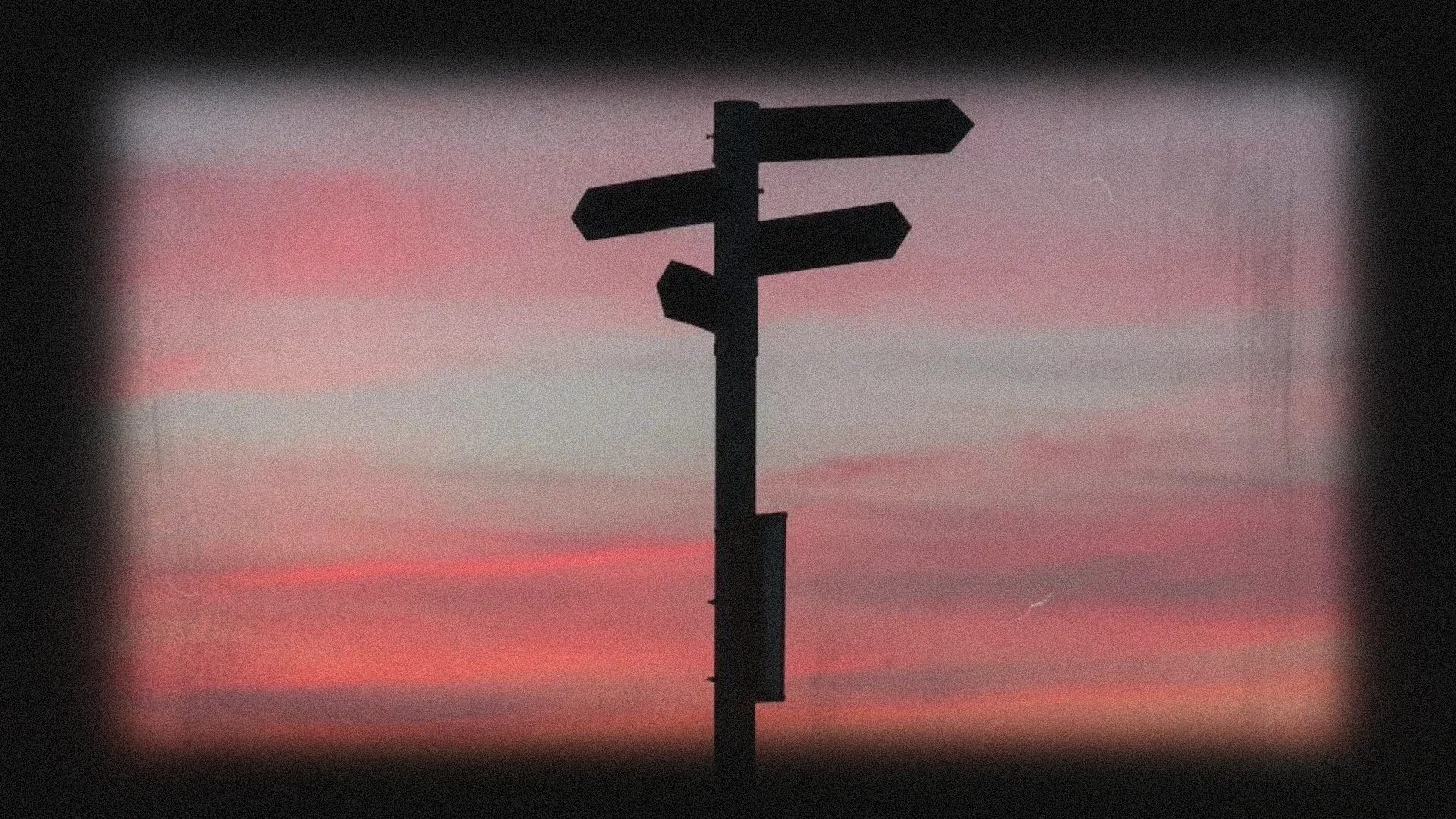 Silhouette of a signpost against a colorful sunset sky.
