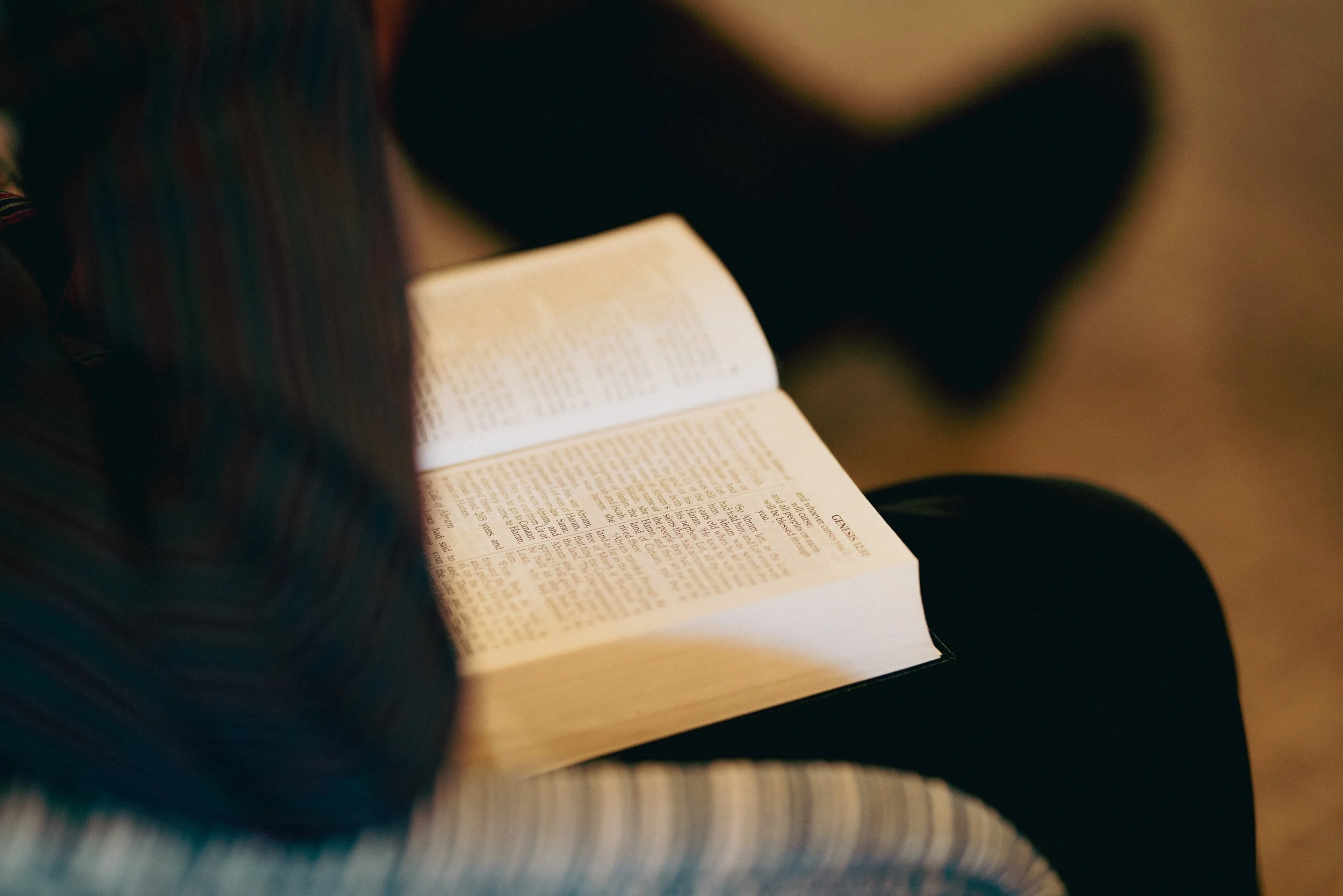 Person reading an open Bible, sitting on a striped upholstered chair.
