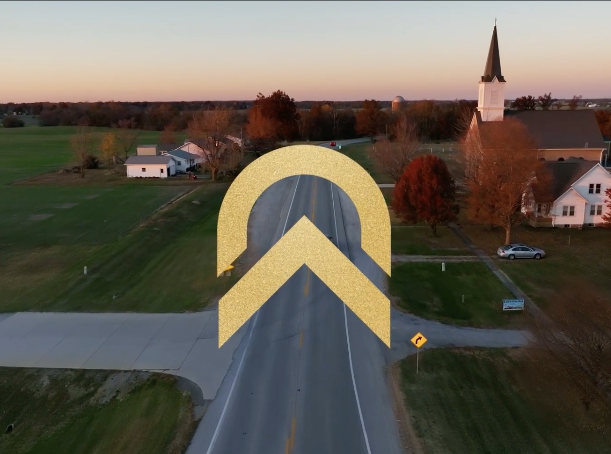 A rural town during sunset with a church and houses, a curved road, and a large gold logo for the LCEF in the center.