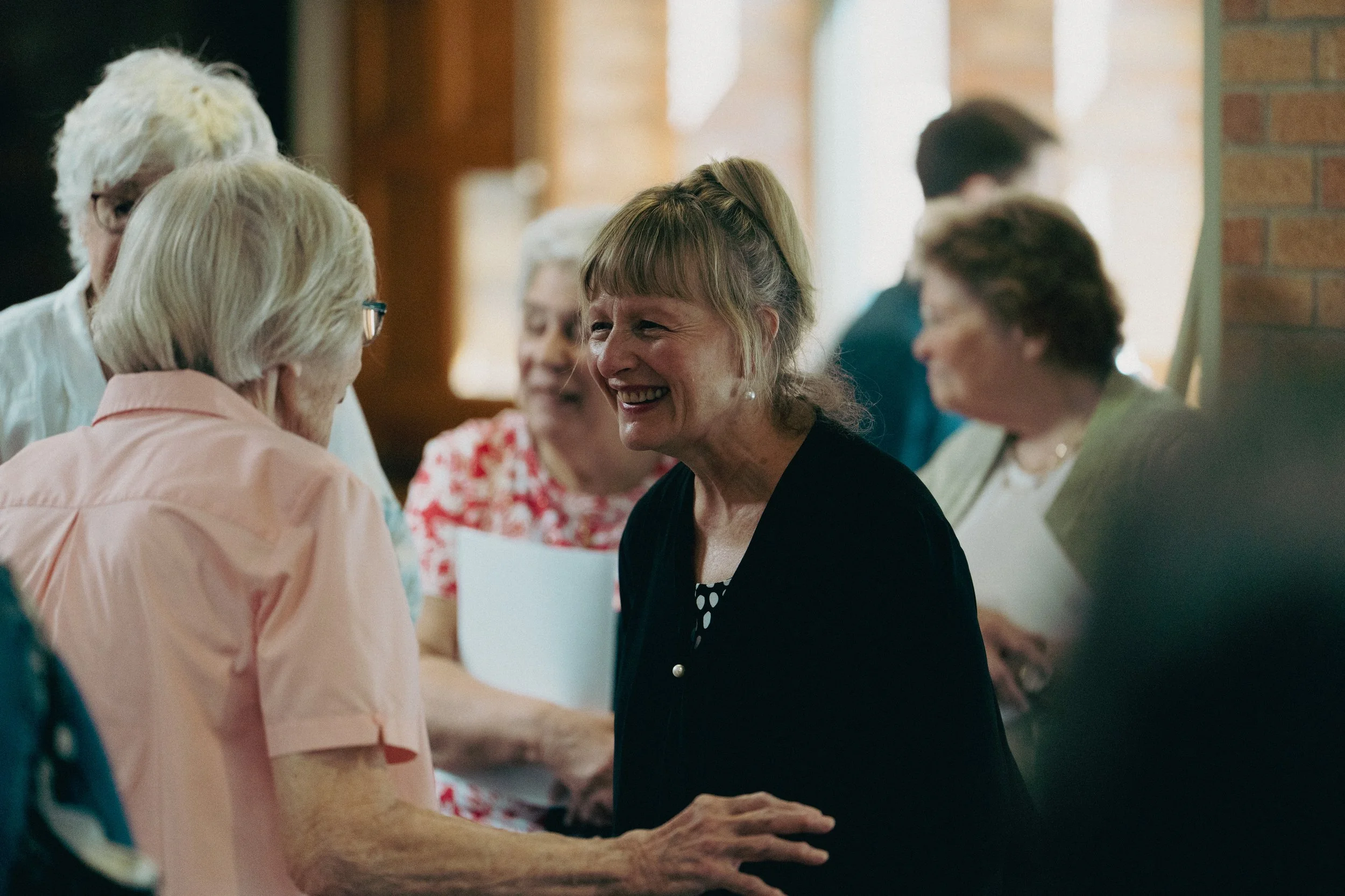 Group of older women talking and smiling in the warmly lit narthex of the church.