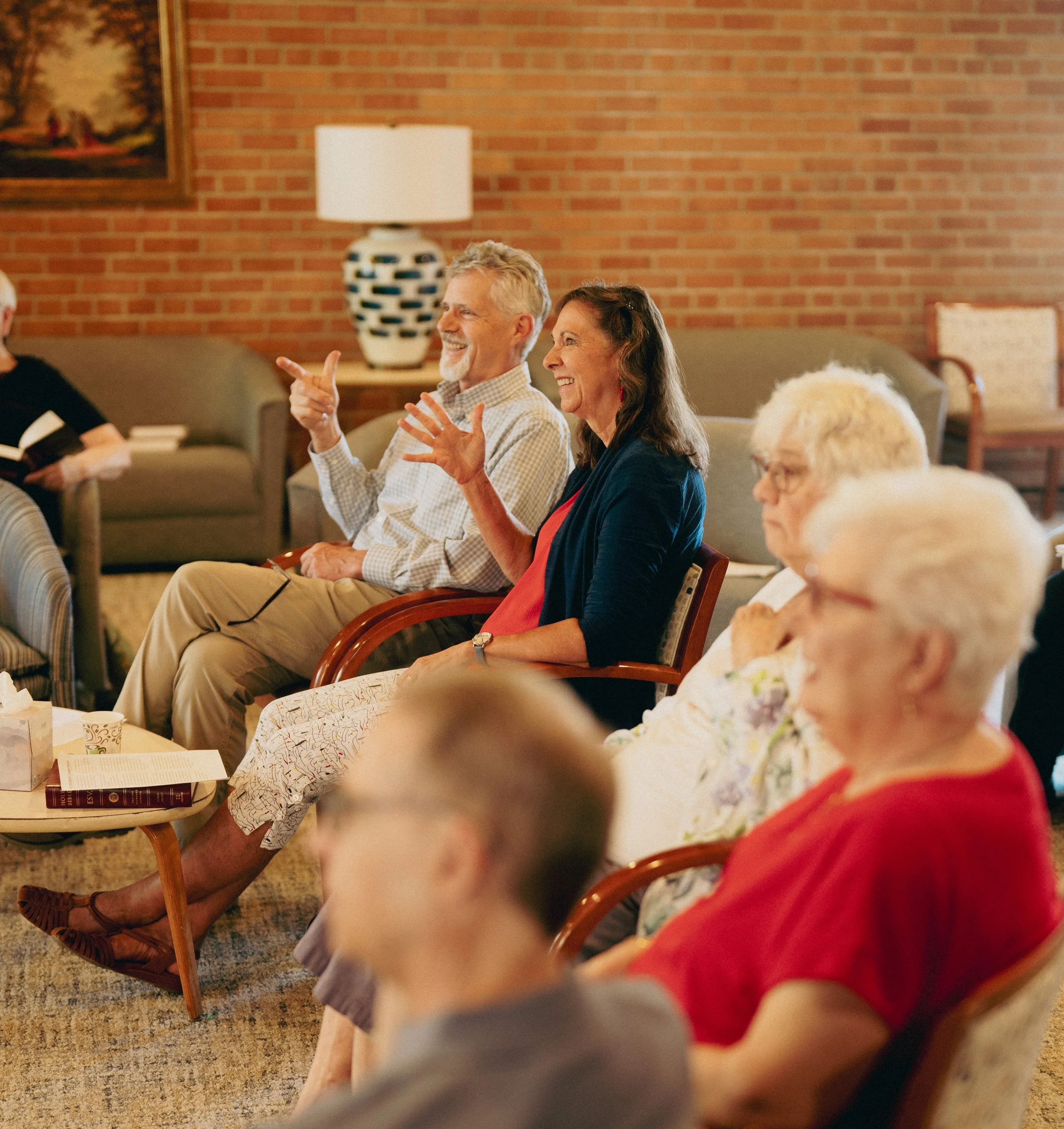 Group of older adults sitting in a living room, smiling and enjoying a social event or gathering.
