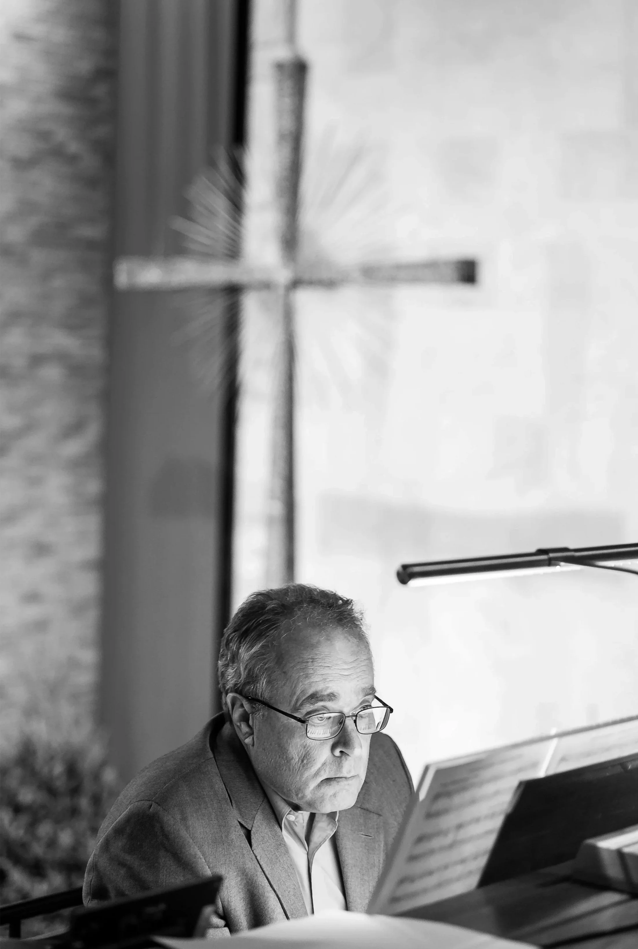 A man with glasses reads sheet music at the organ with a large cross hanging above the altar behind him.