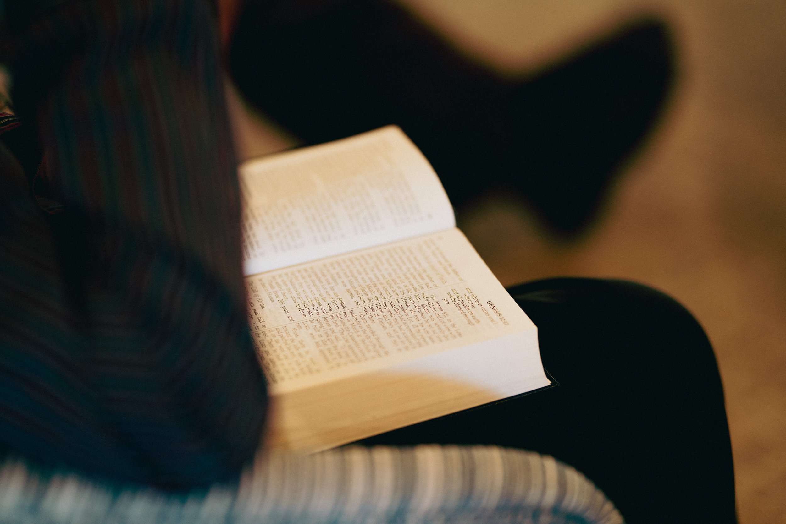 A person reading a Bible, seated on a striped chair with the focus on the open pages.