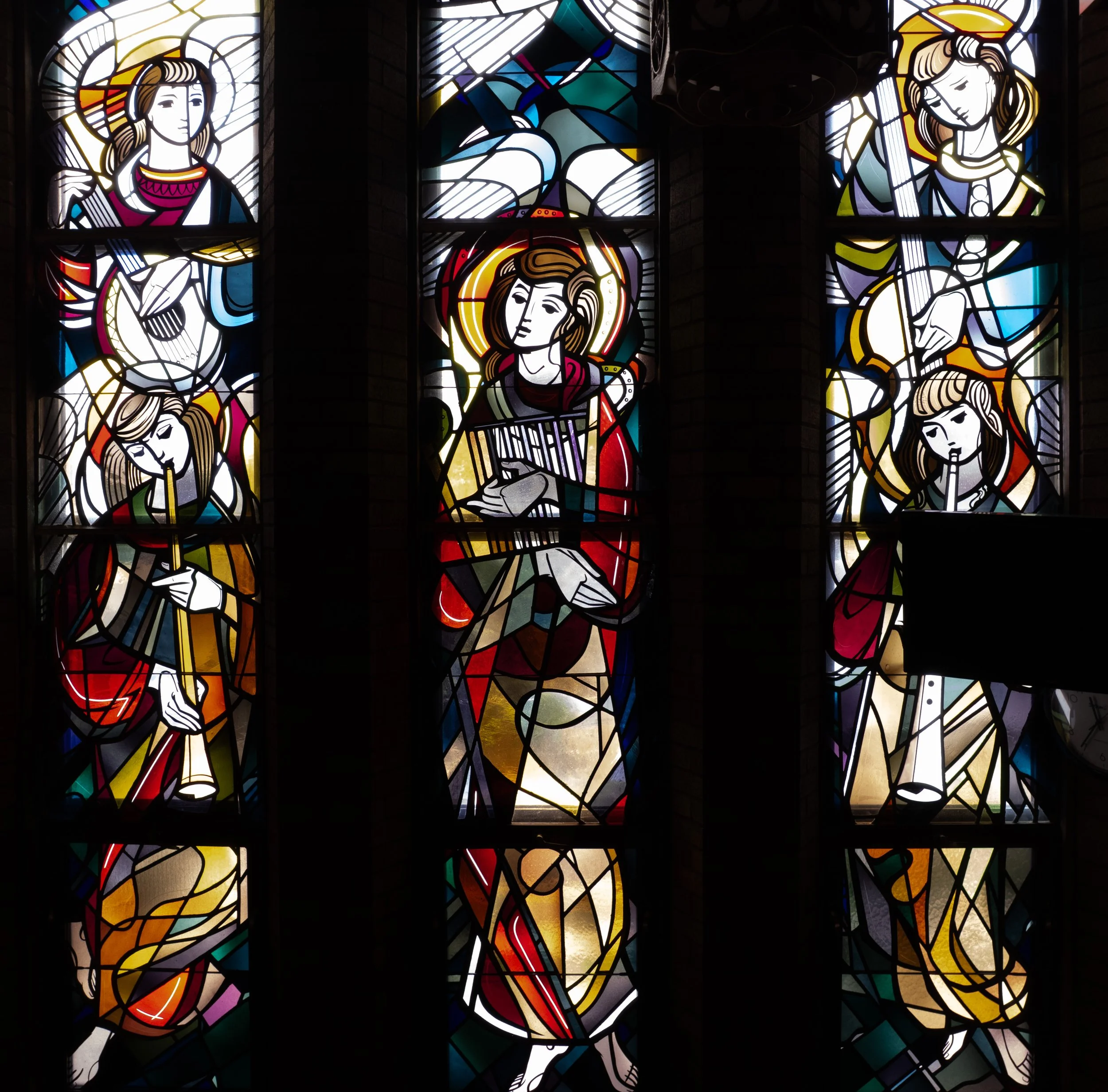 Colorful stained glass window depicting religious figures playing musical instruments, with some figures holding guitars and others with halos around their heads.