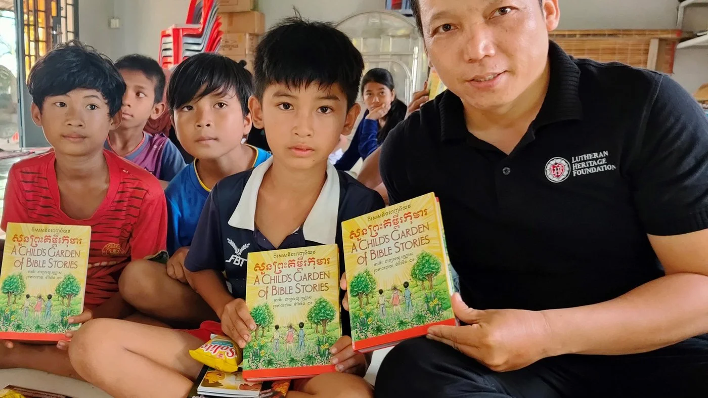 A man and four children sitting together indoors, holding books titled 'A Child's Garden of Bible Stories' with a colorful cover illustration of children and trees.