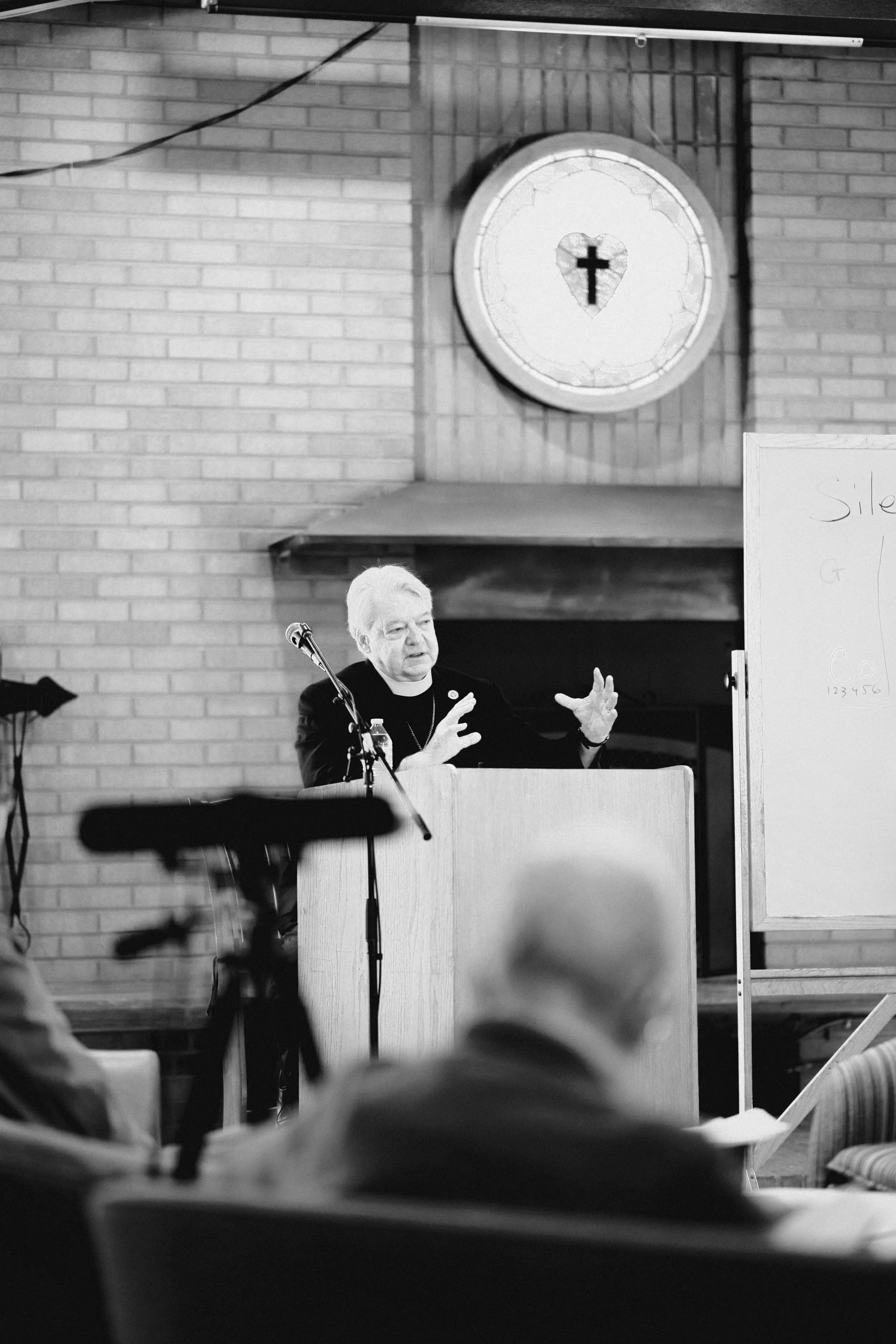 A pastor giving a leading bible study at a podium in a church, with a whiteboard to his side.