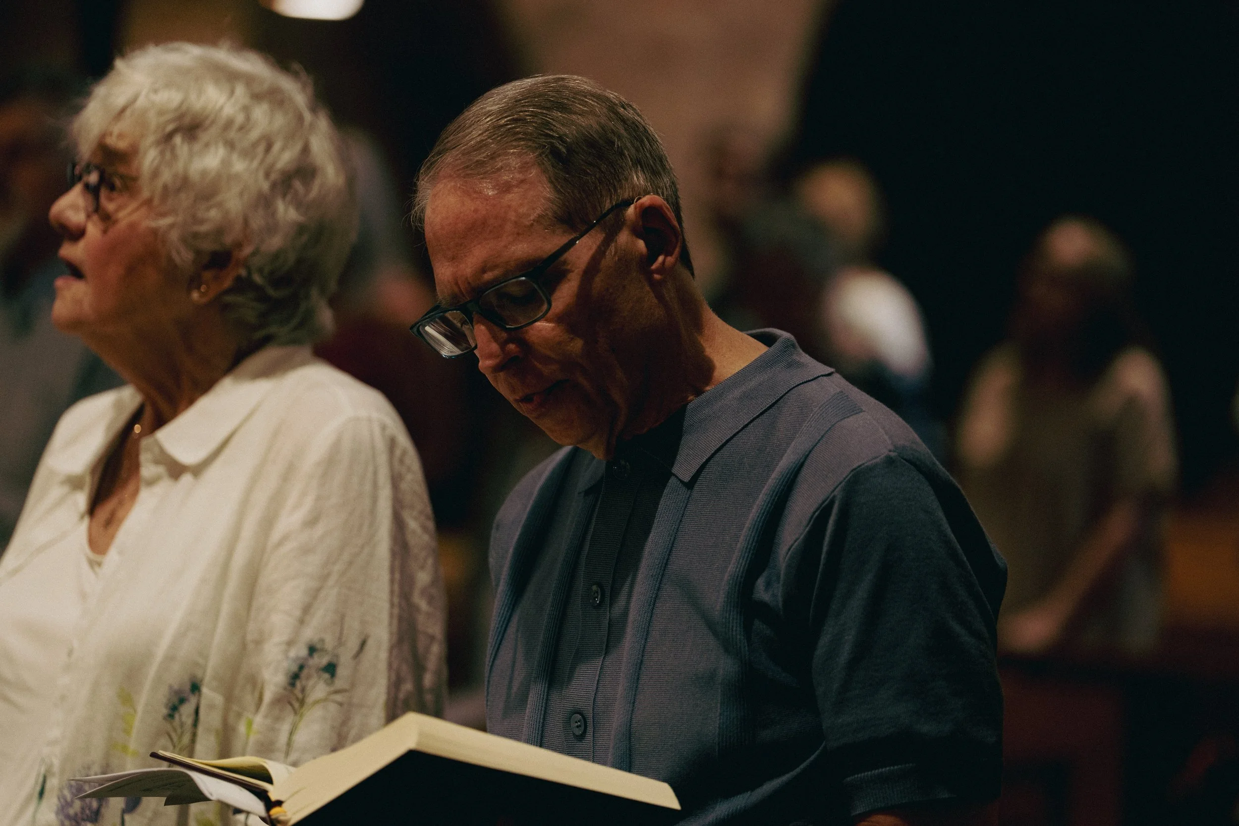 A man and woman standing in prayer in a church, with other people in the background.