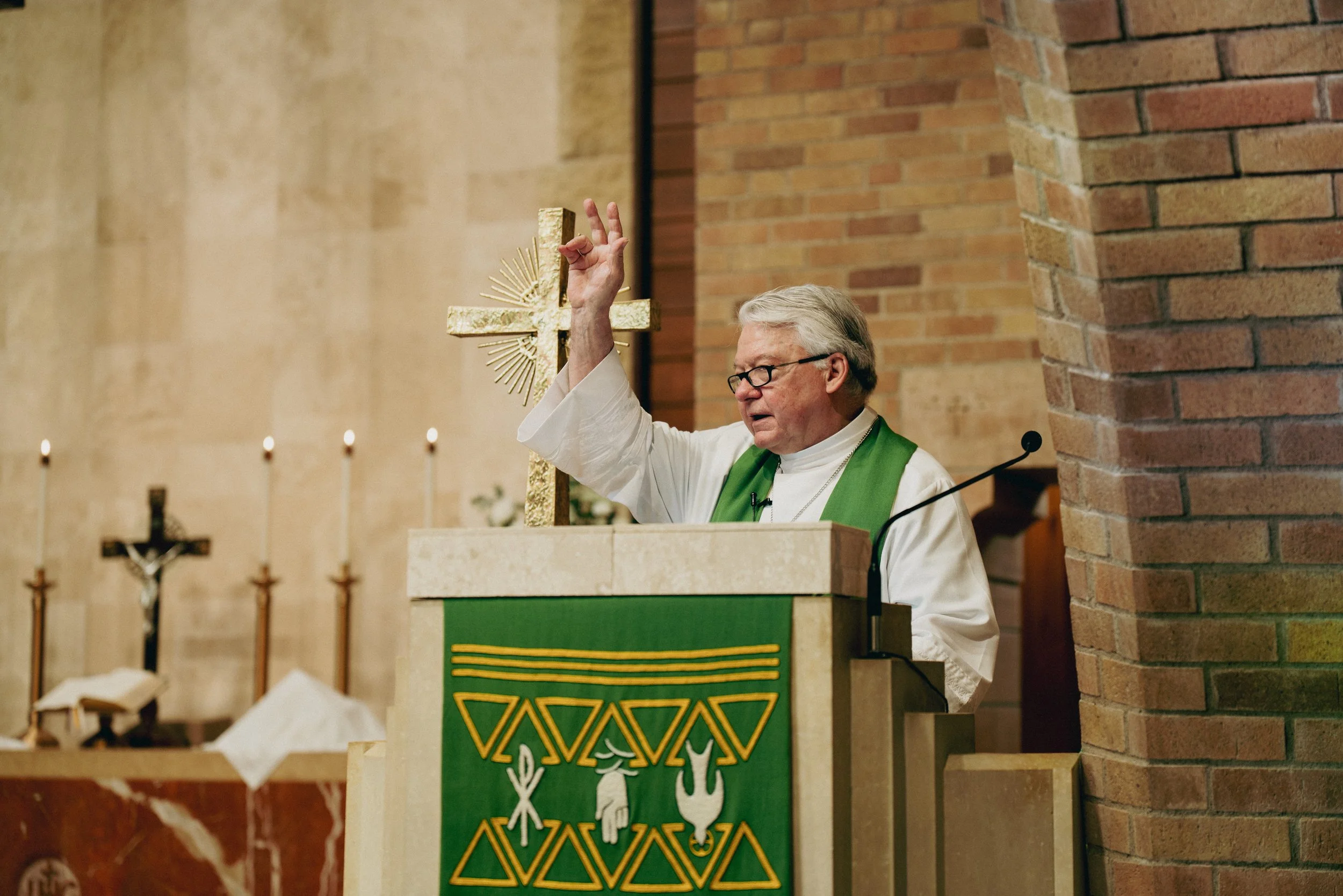 A pastor with a raised hand, gives a cross gesture to bless the congregation after ending his sermon at the pulpit.