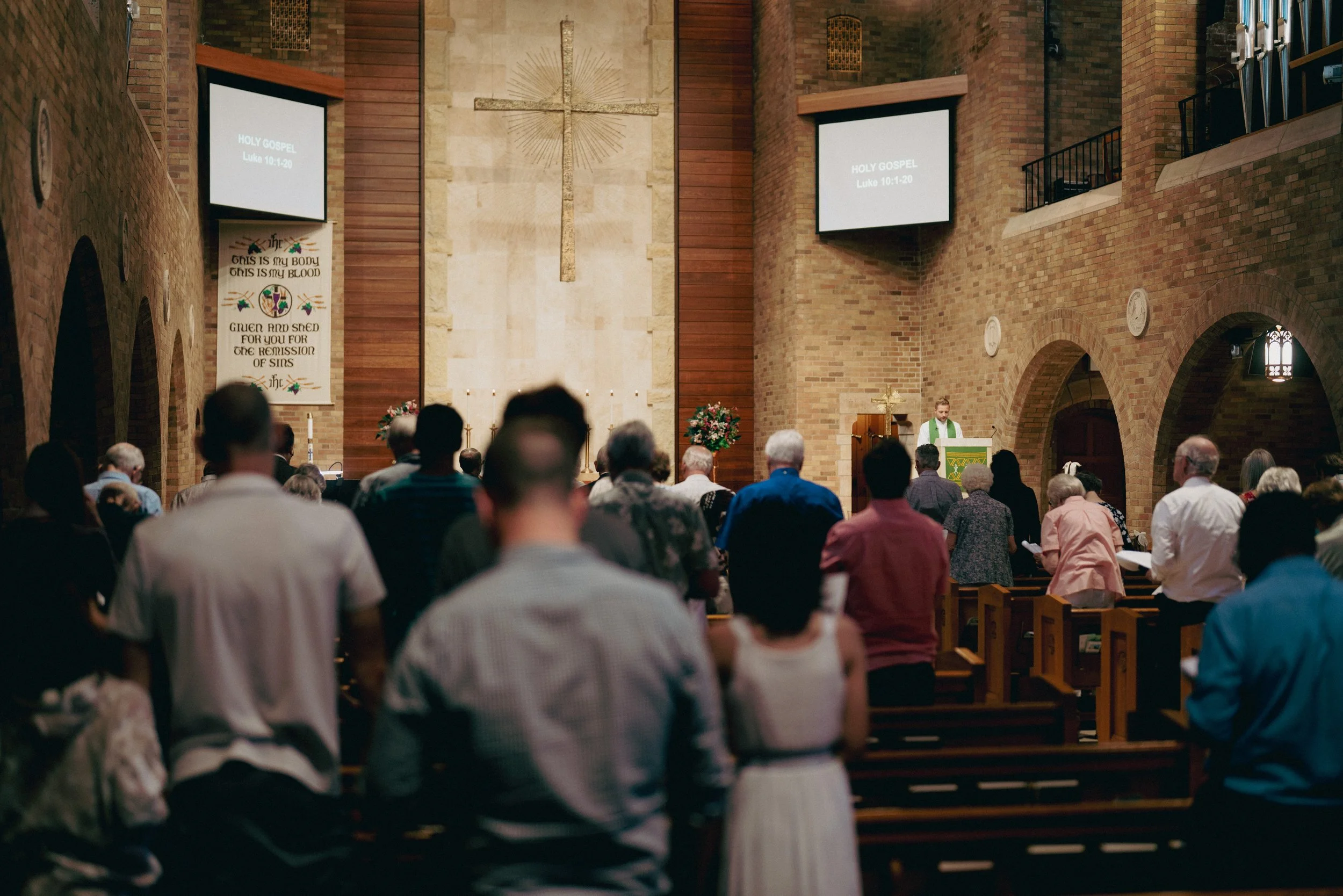 Inside a church with brick walls, a congregation is gathered for a service.
