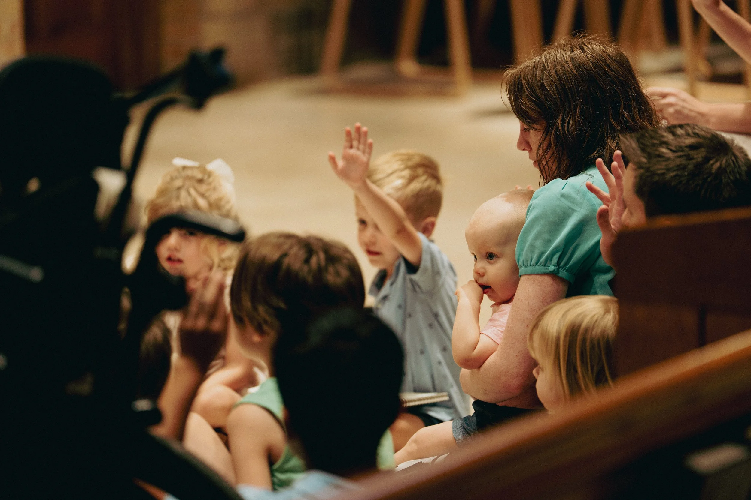 Kids sitting on the floor during the children's message with a woman holding a baby and a child raising their hand.