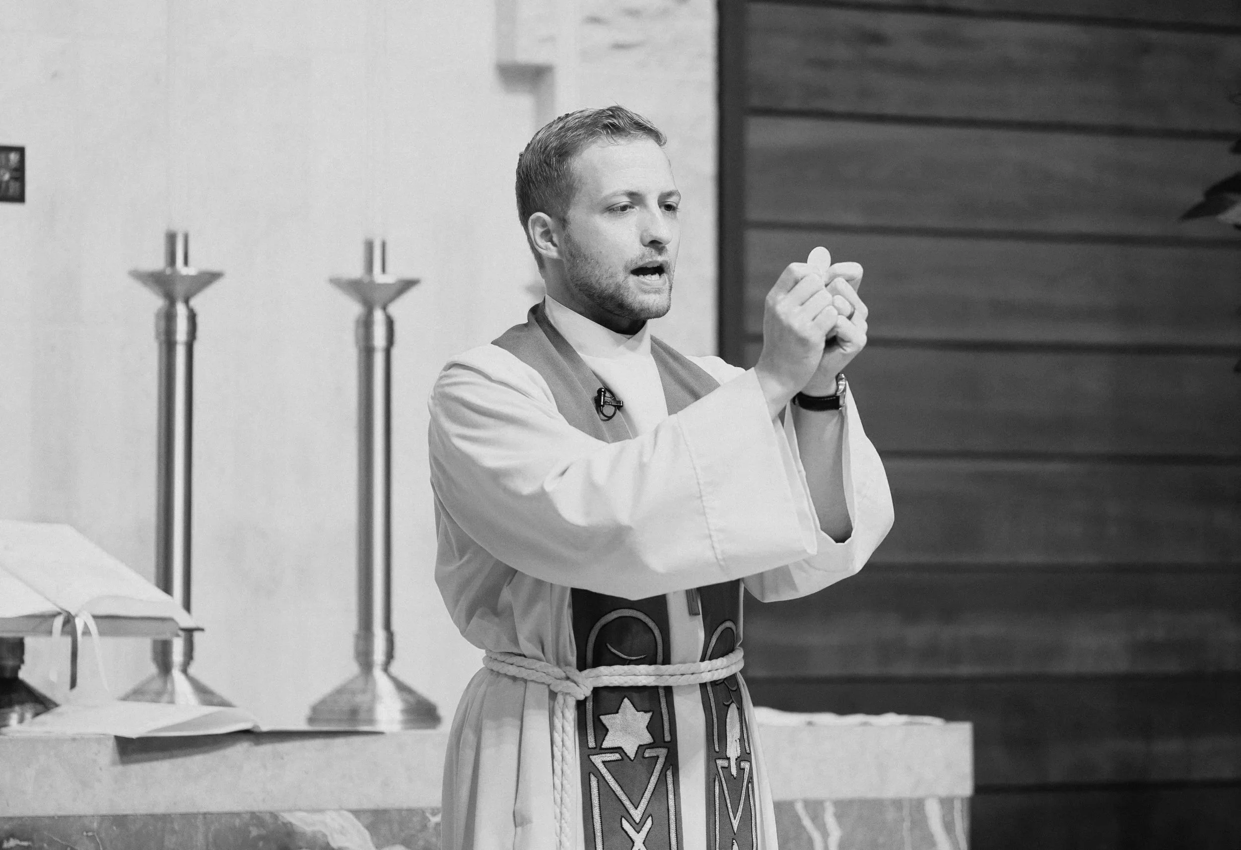 Black and white photo of a pastor in robes standing at the altar holding up the Eucharist.