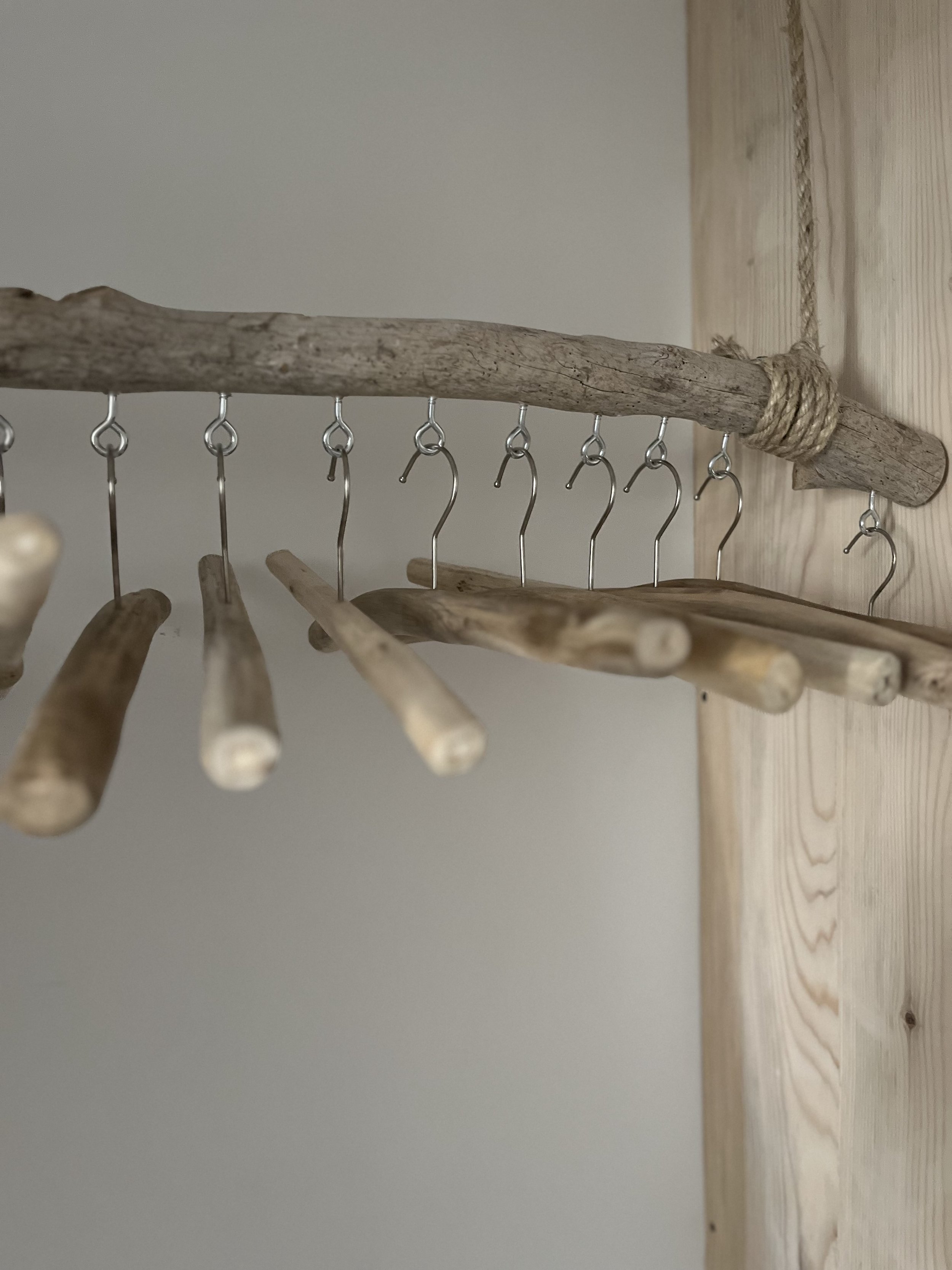 Wooden hangers hanging on a rustic wooden rod suspended from a nail on a wooden wall.