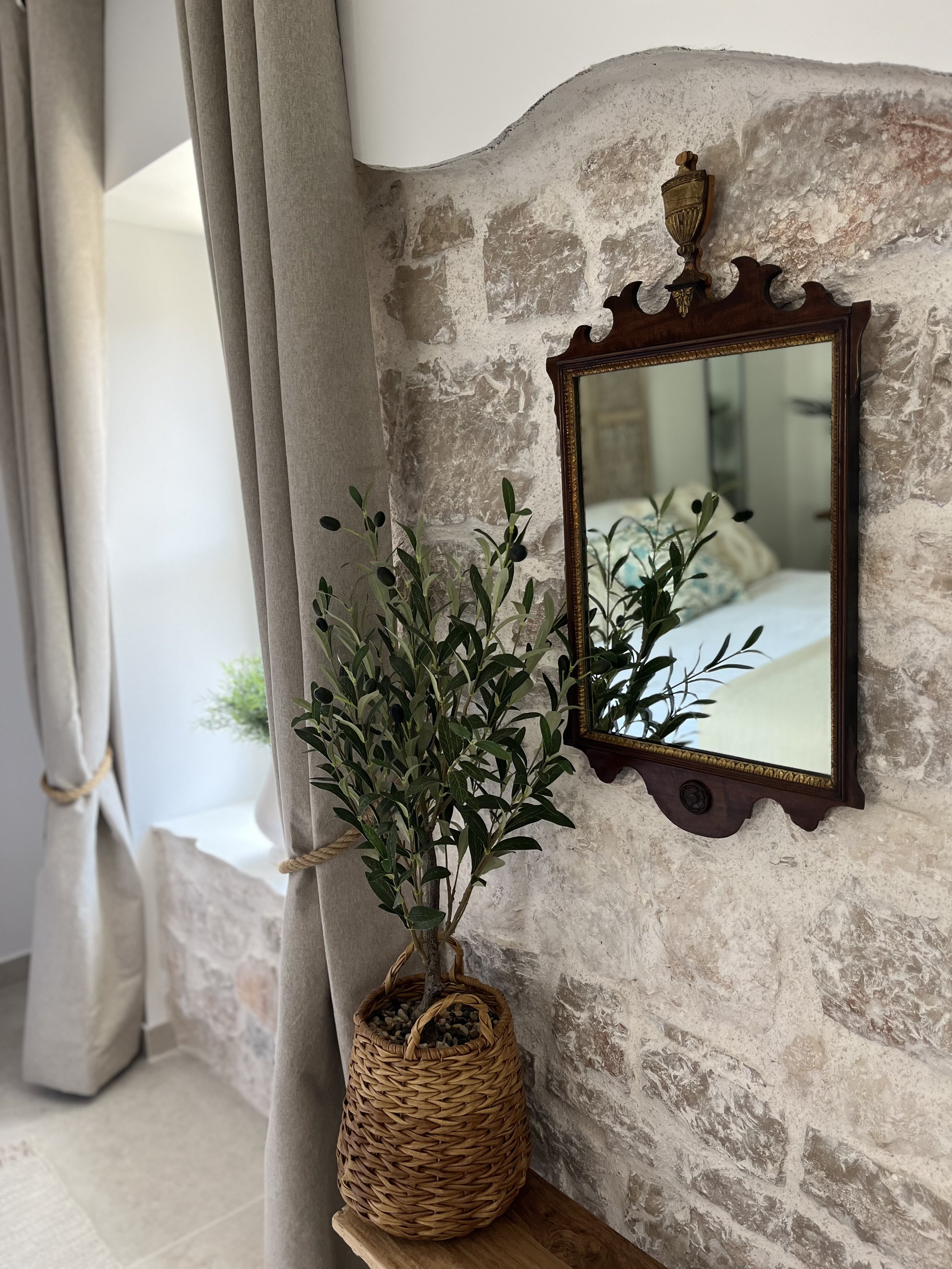 Decorative interior with a vintage mirror and potted plant near a textured stone wall.