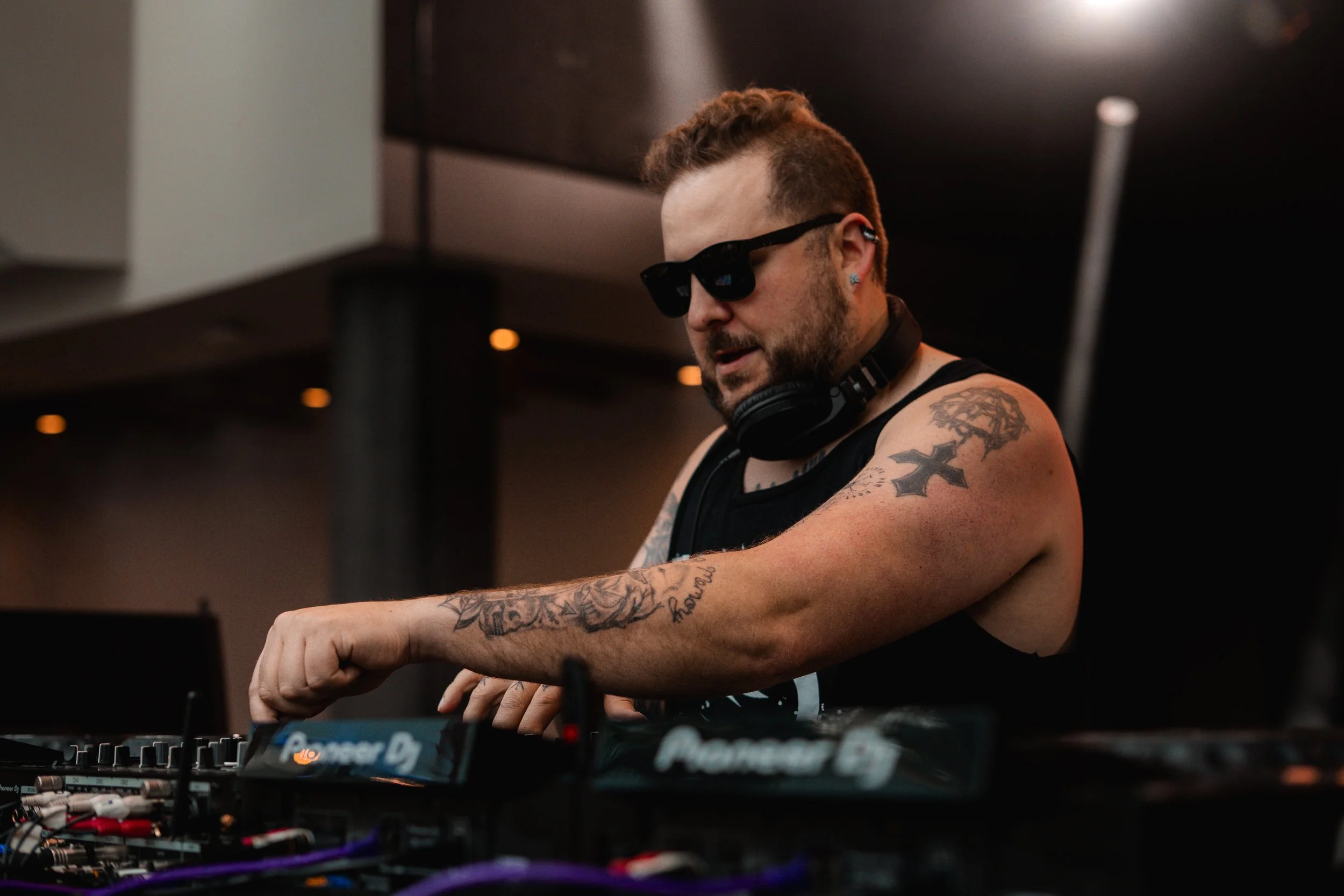 A DJ with tattoos, mattb and collin chaos console in a dark club environment. artist prominent dj grand rapids ready for bookings and big festivals, artist, founder remedy collective djs sound production morris media byron morris