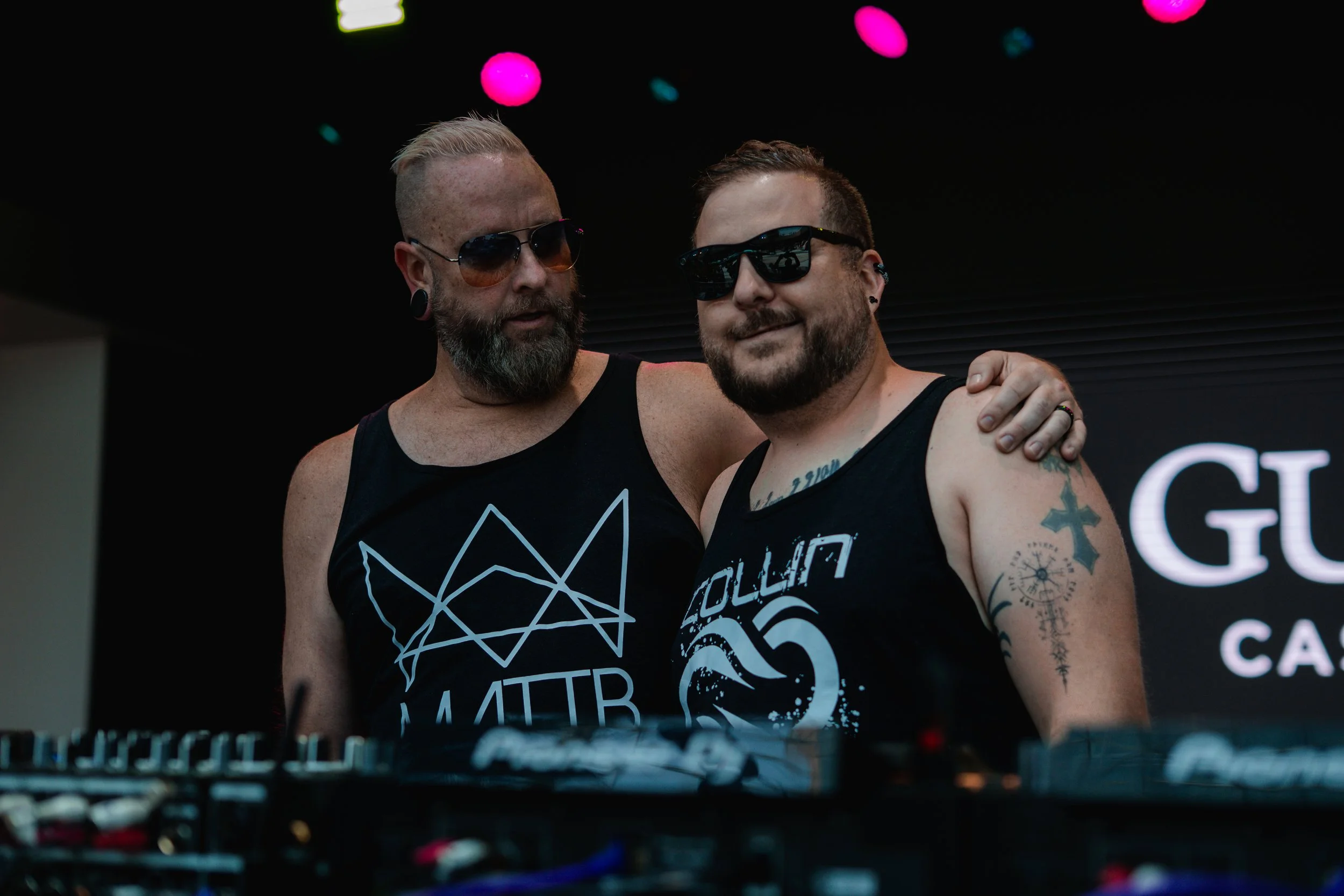 A DJ with tattoos, mattb and collin chaos console in a dark club environment. artist prominent dj grand rapids ready for bookings and big festivals, artist, founder remedy collective djs sound production
