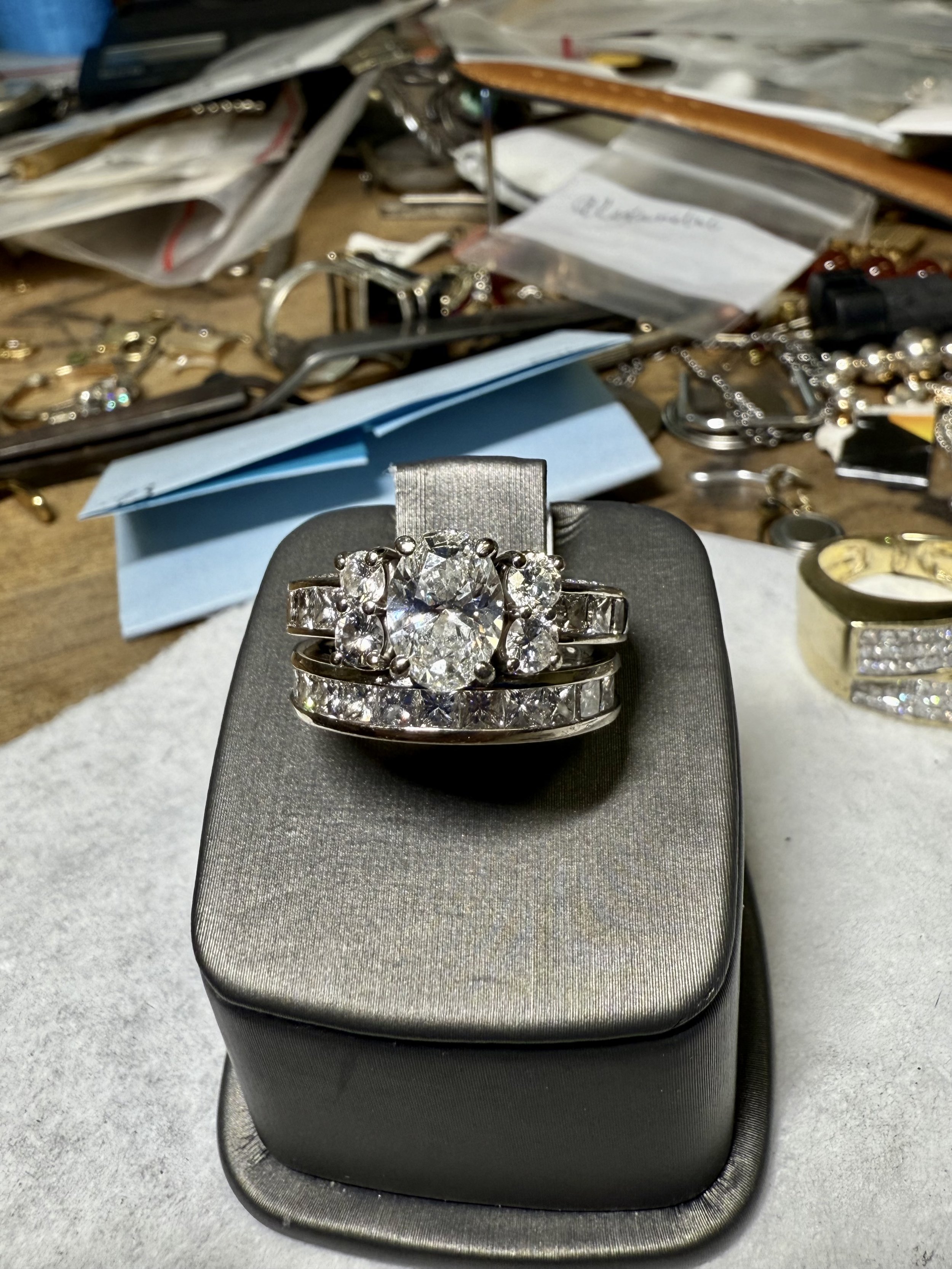 Set of diamond rings on a jewelry display stand with disorganized jewelry pieces and documents in the background.