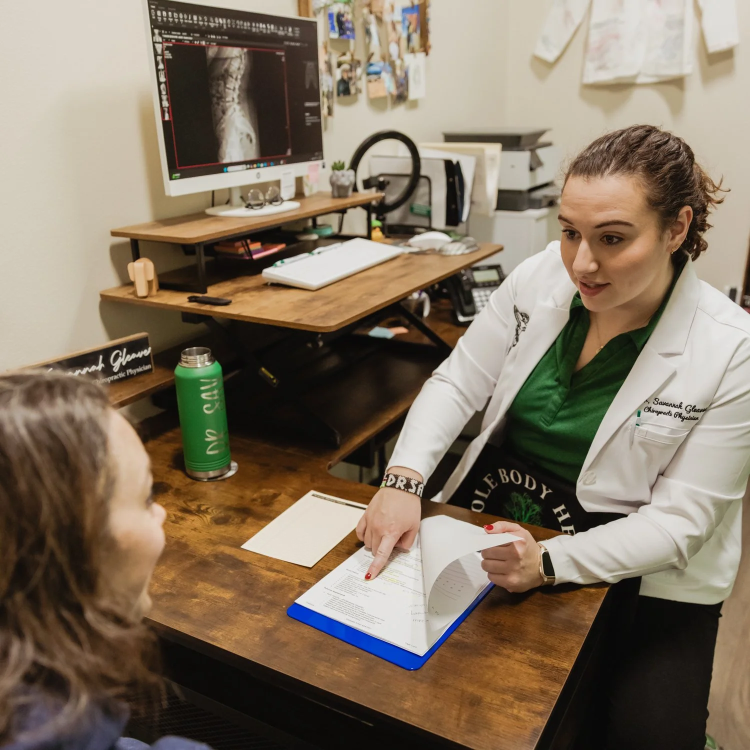 A female chiropractic doctor explaining the personalized and recommended treatment plan to a new patient in an office with a computer monitor and office decor.
