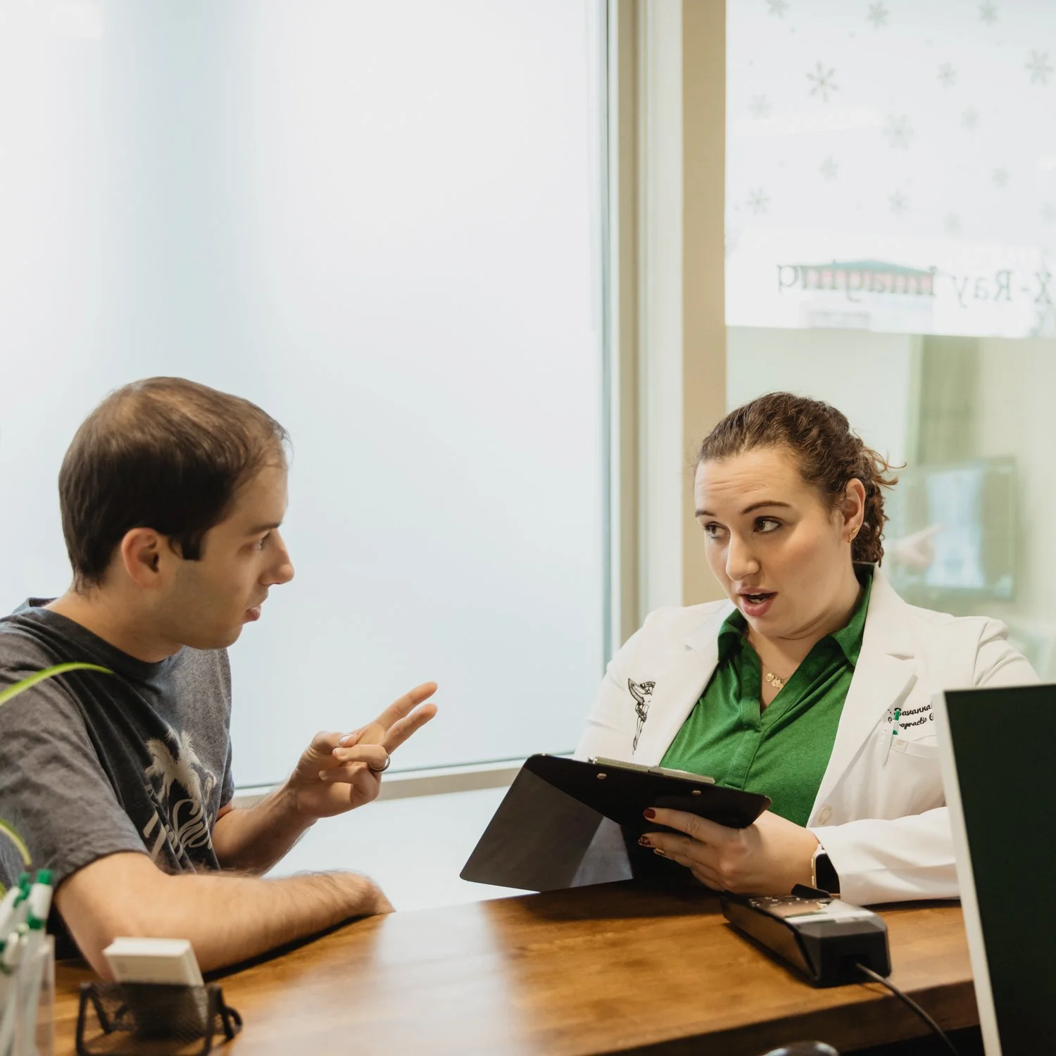A young man and a chiropractic doctor having a conversation. The doctor is wearing a white coat, and the young man is making a peace sign with his fingers.