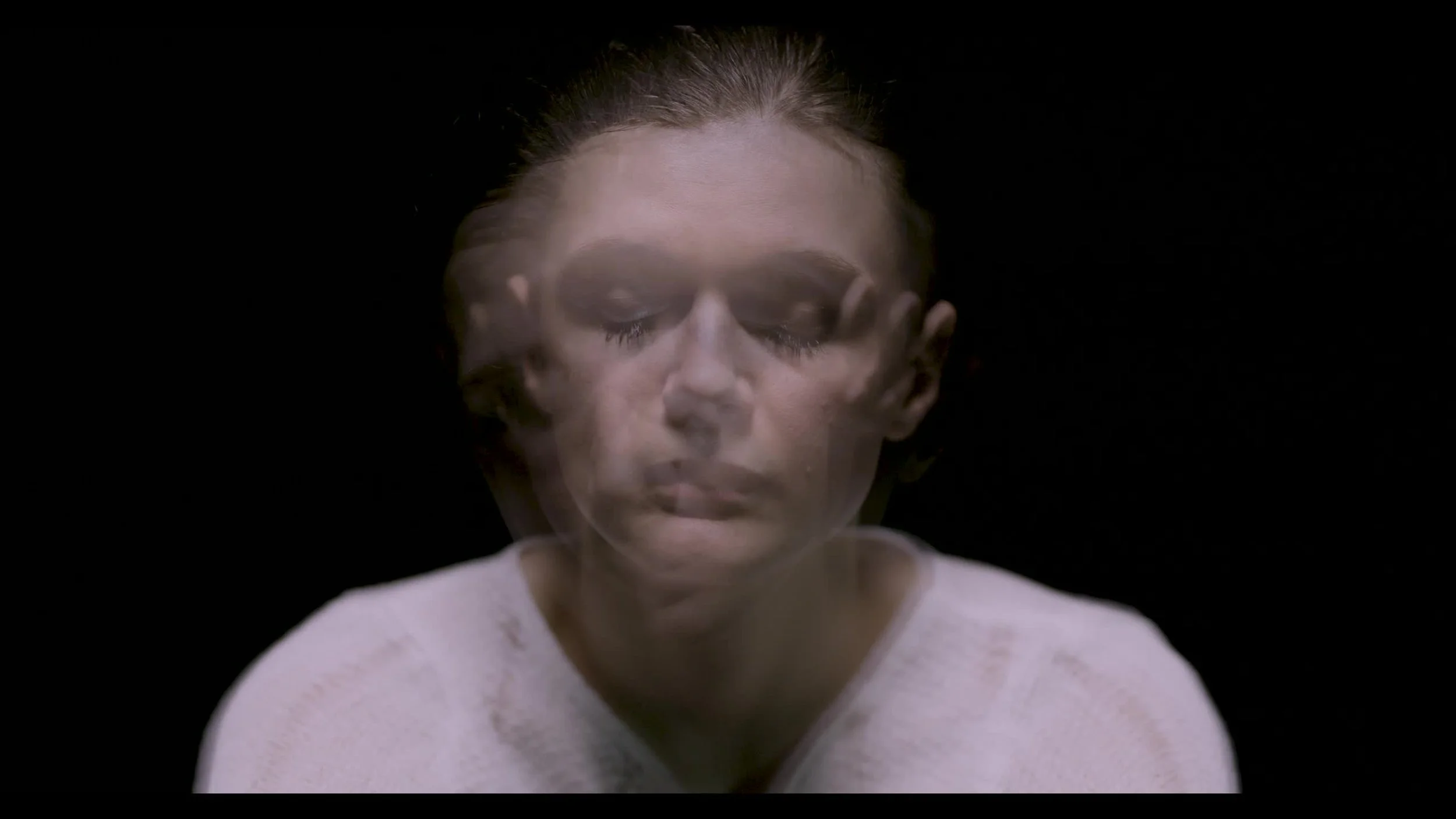 A person with closed eyes, wearing a white top, appears to have a layered or double exposure effect against a black background.