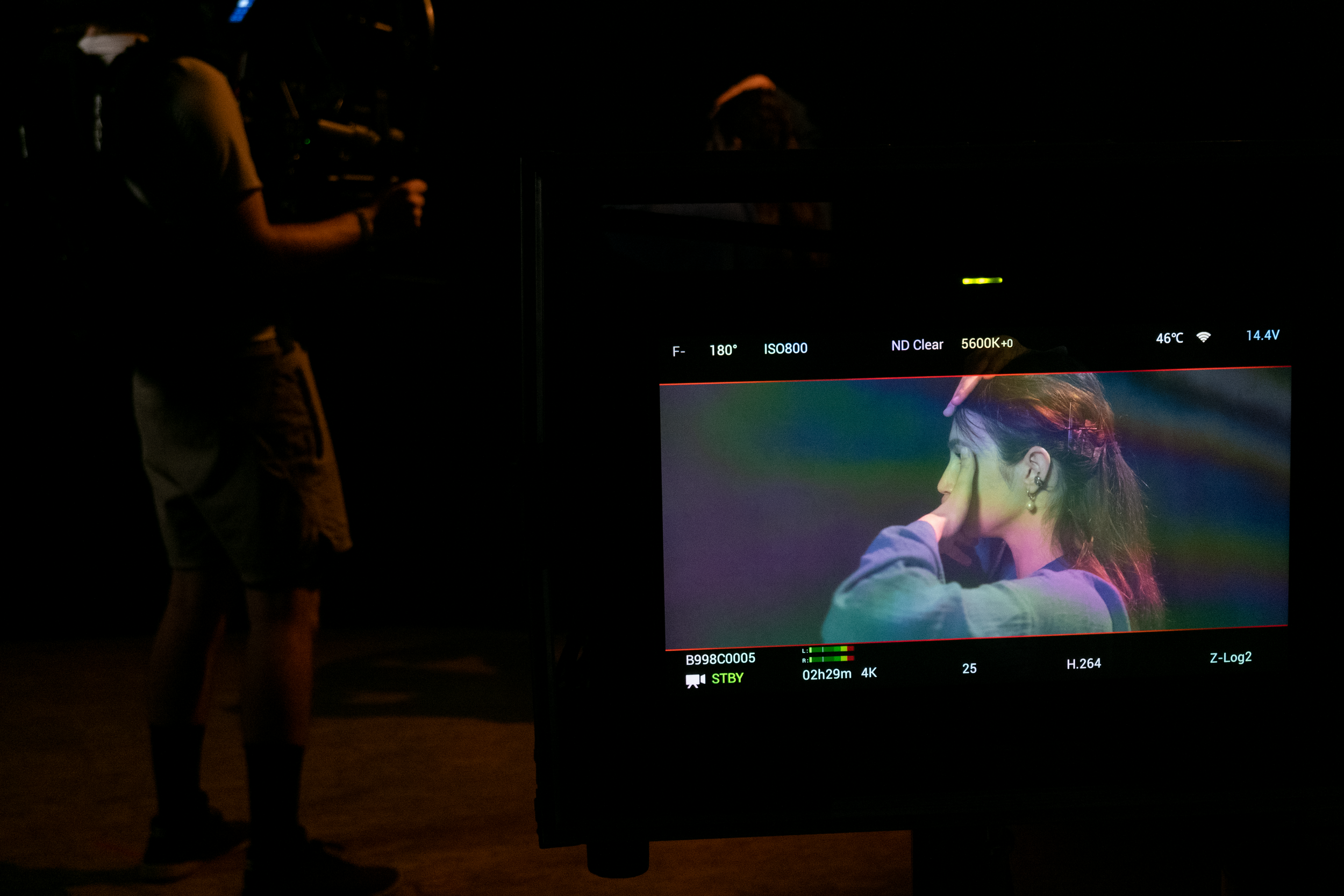 A video producer or director working on a film set, with a monitor displaying a woman's portrait against a colorful background.