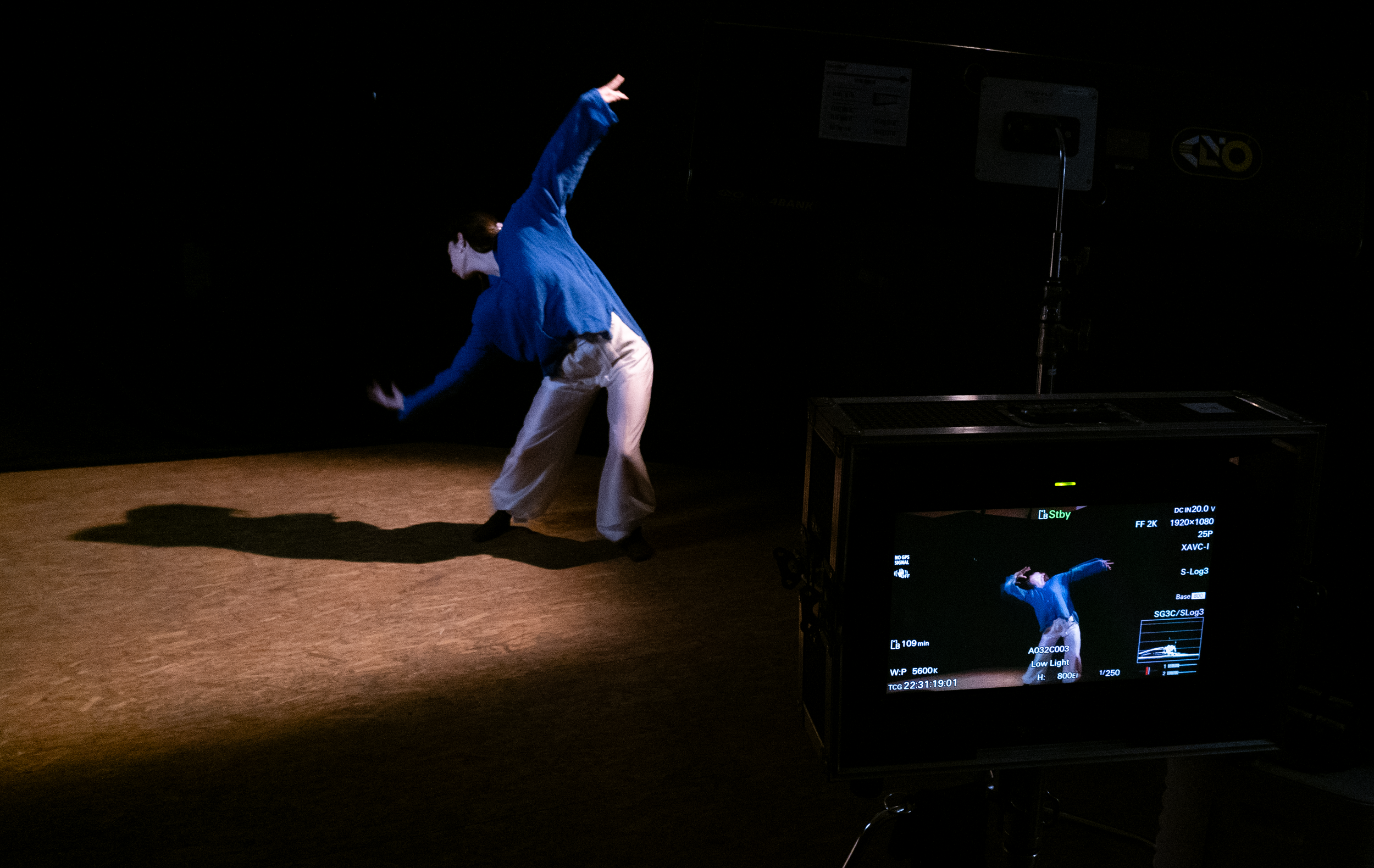 Person performing a dance move in a dark studio, filmed on a monitor during a recording session.