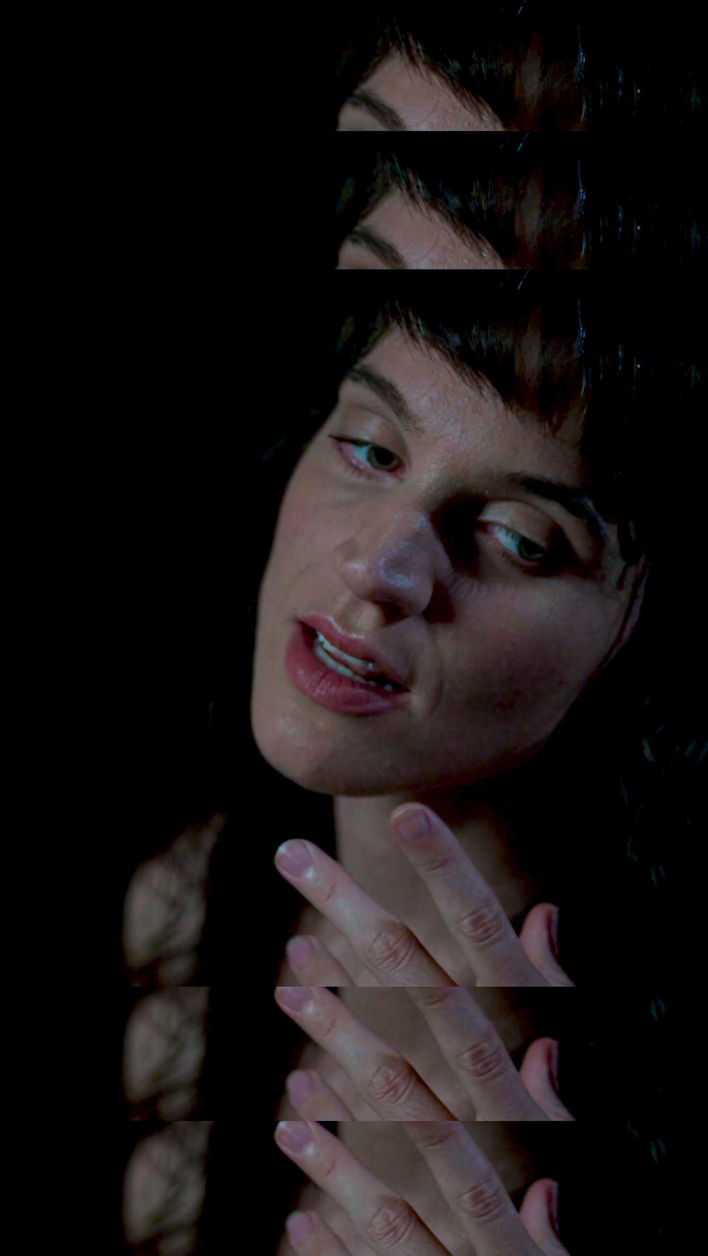 A woman with black hair and light skin making a playful or flirty expression, with her tongue slightly out and fingers near her chin, against a dark background.