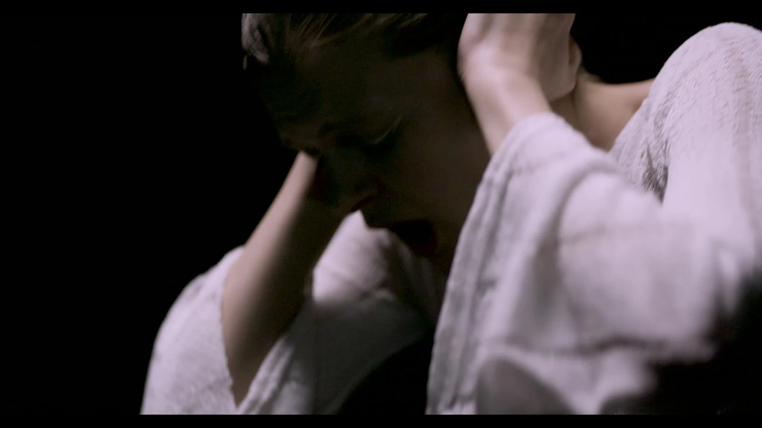 A woman with short hair is holding her head with both hands in a dark setting