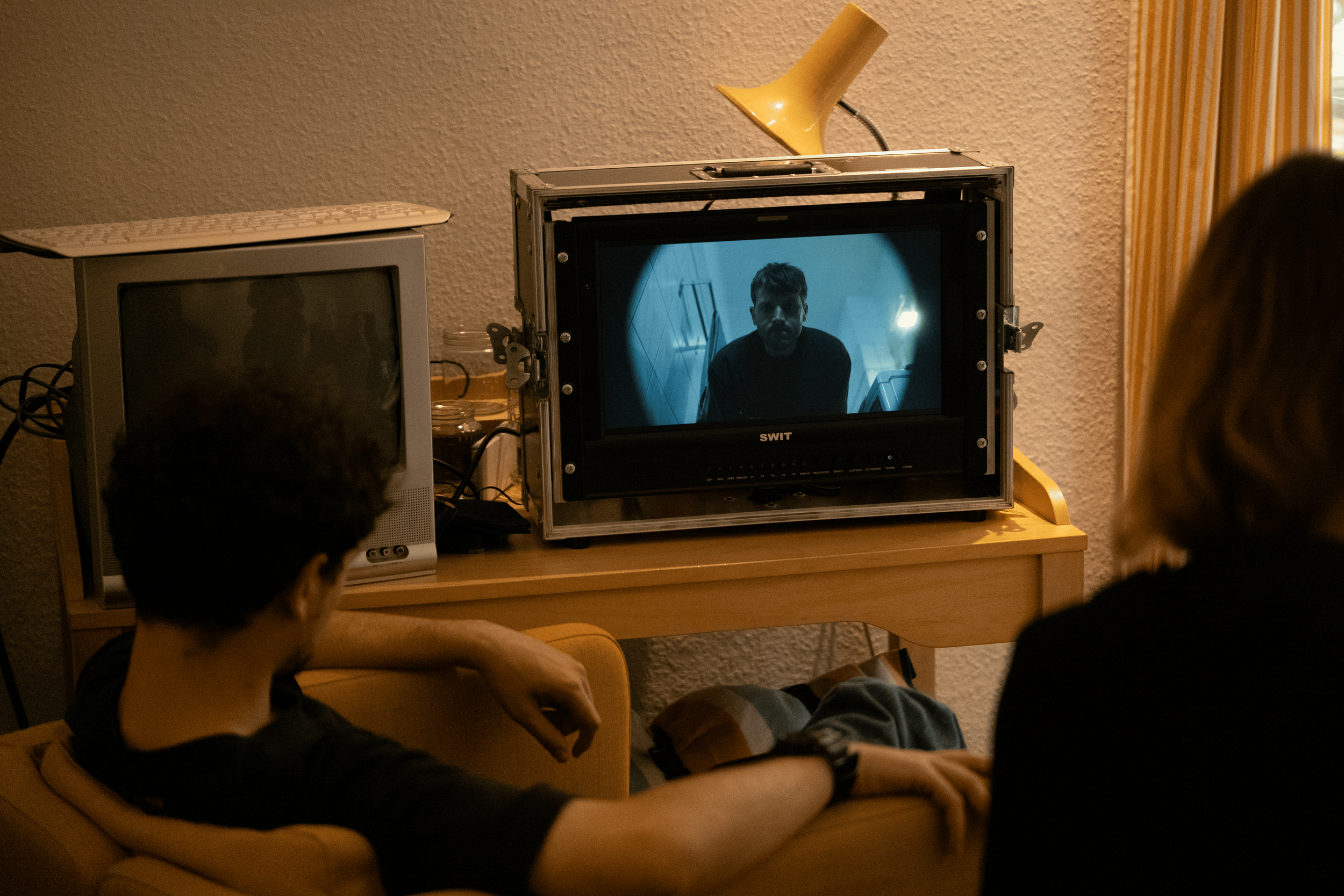 Two people watching a television with a black-and-white film of a man looking up at the camera.