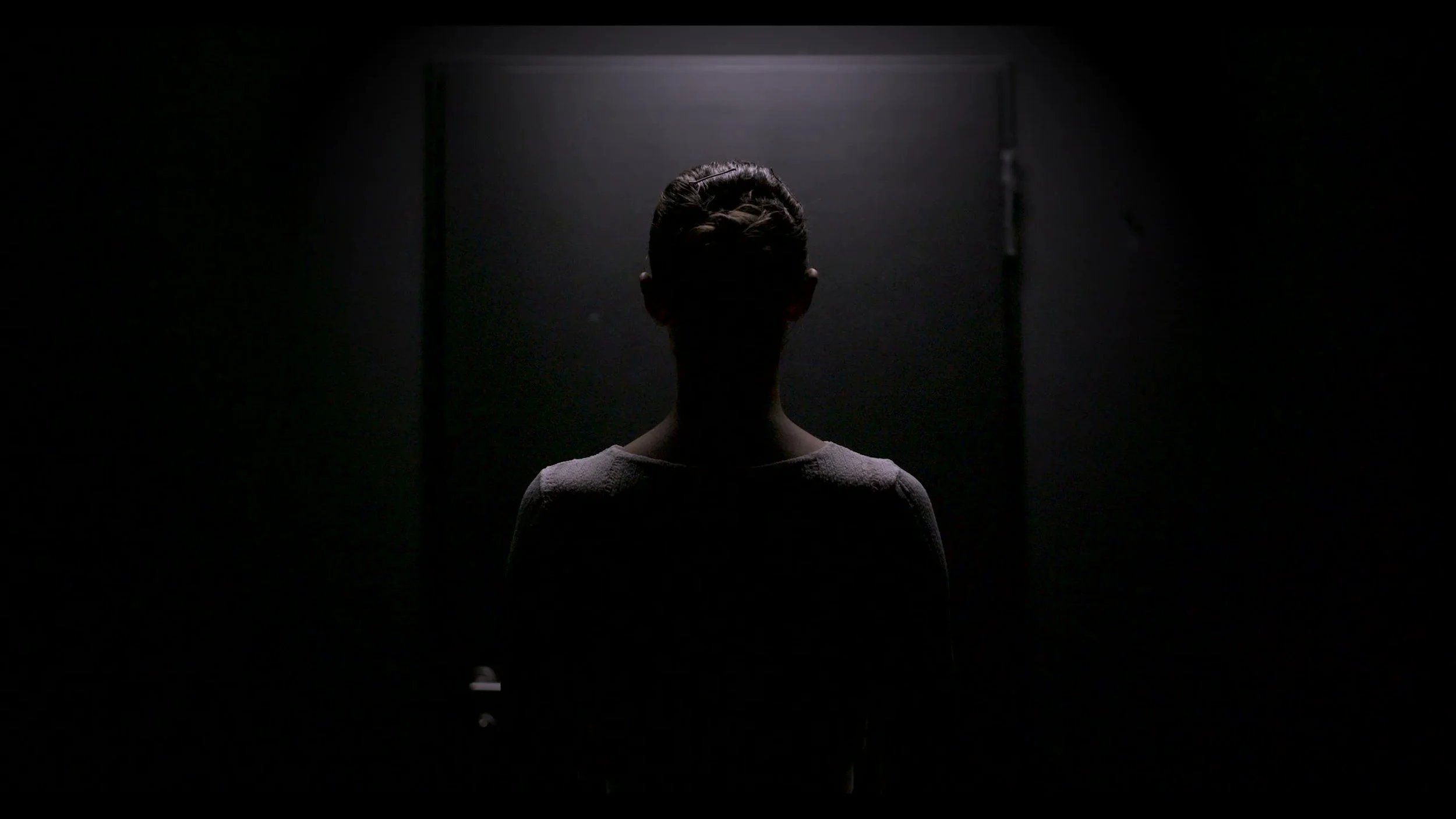 Silhouette of a person standing in front of a bright light in a dark room.