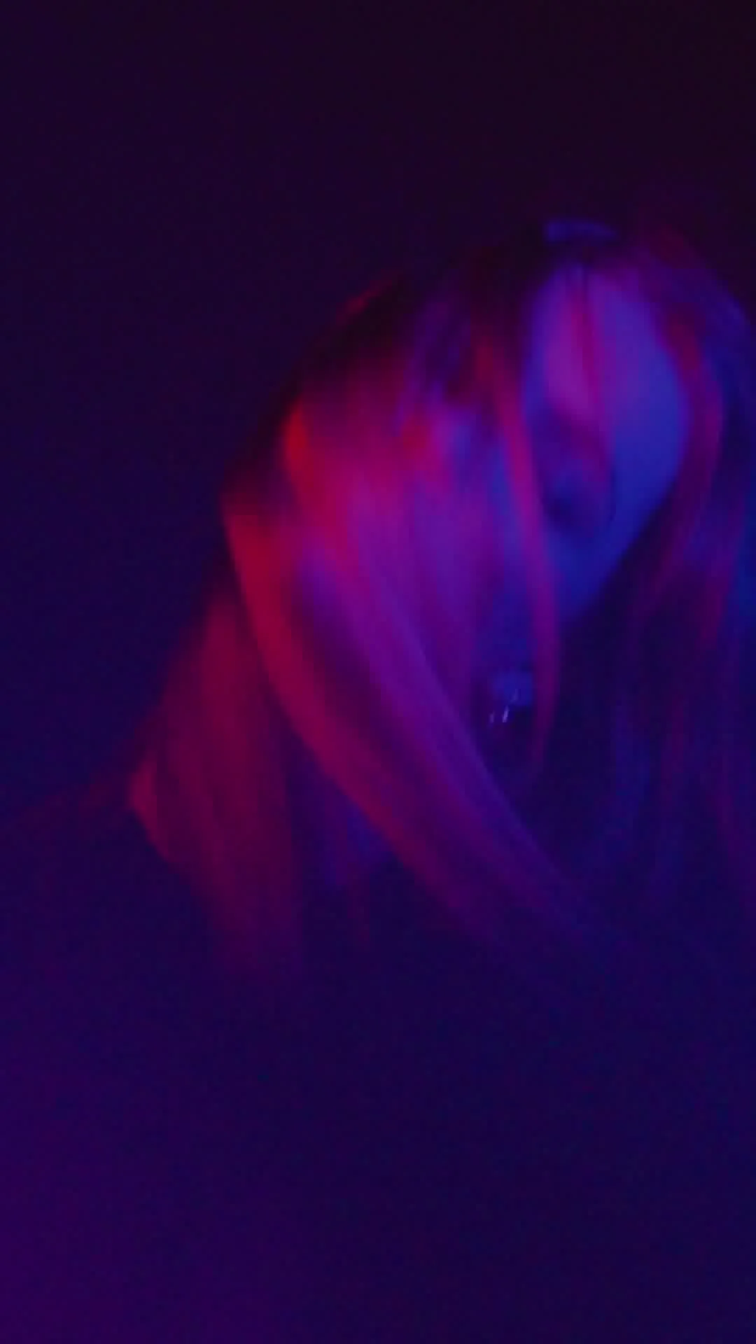 Close-up of a person's face with vibrant purple and pink lighting in a dark setting.