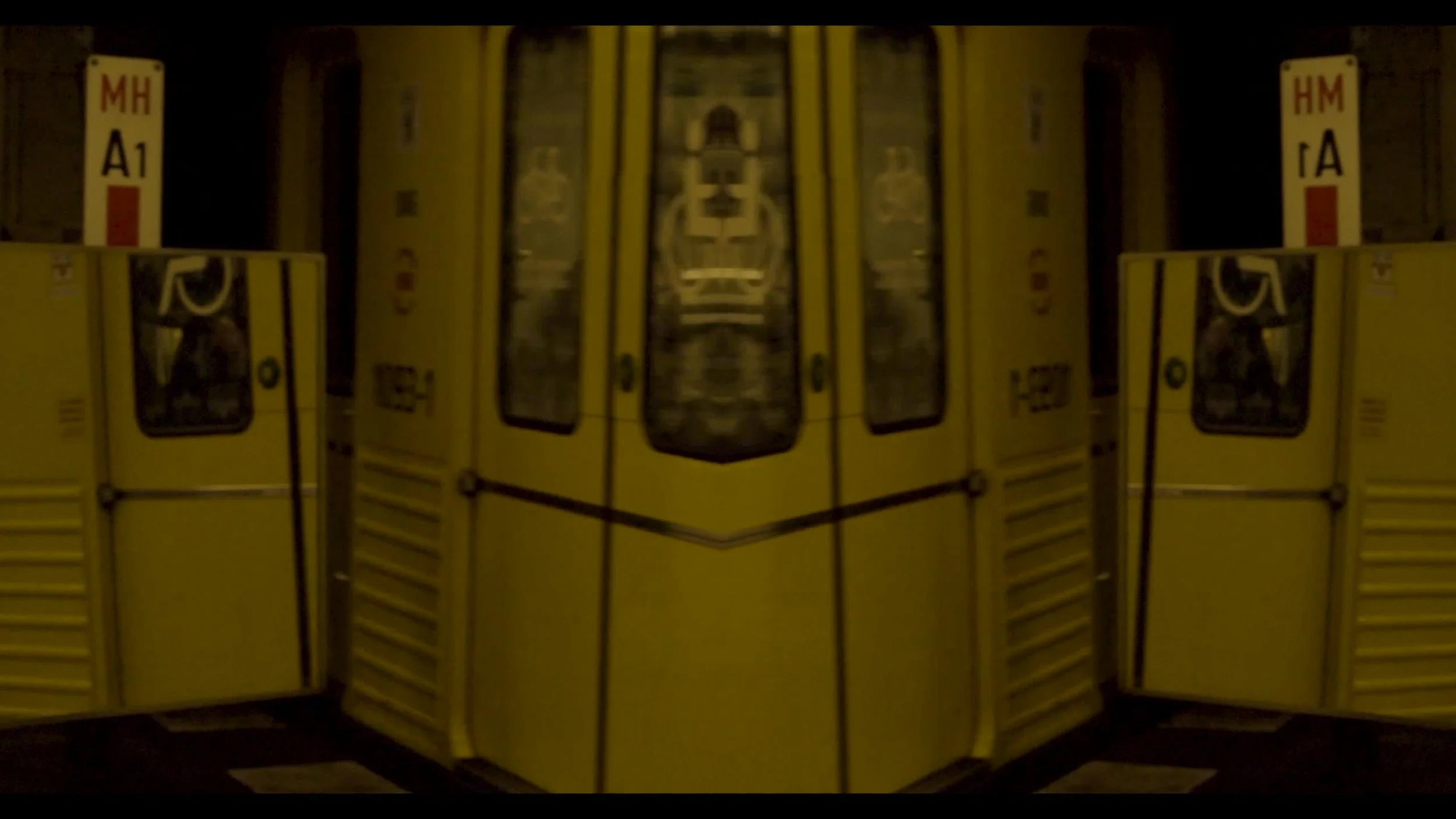 Yellow airport luggage carts with windows, placed side by side, reflecting in a mirror, creating a symmetrical appearance.
