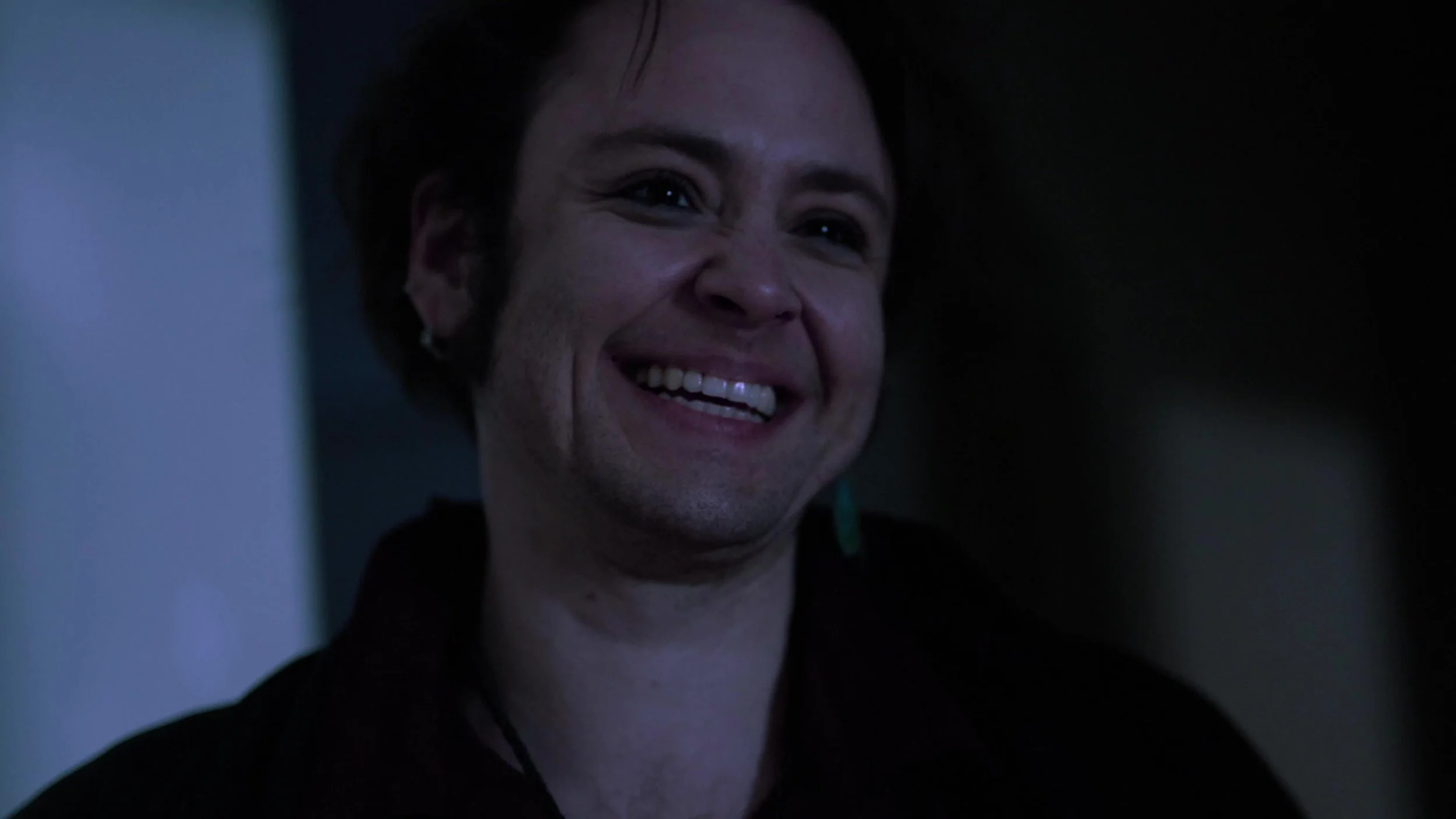 Close-up of a woman smiling with a joyful expression, dark background, and soft lighting.